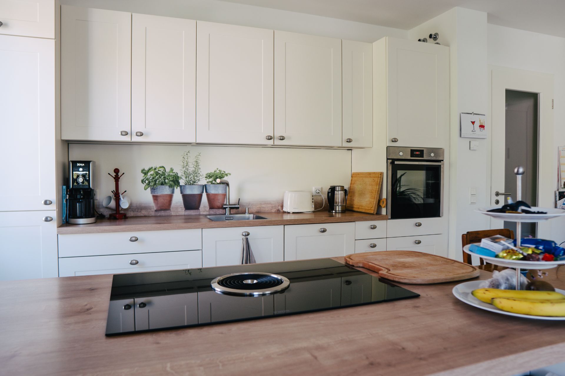 Moderne Küche mit weißen Schränken, Kochfeld, Ofen und mehreren Küchengeräten auf der Arbeitsfläche.