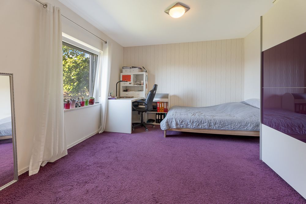 Helles Schlafzimmer mit lila Teppich, Bett, Schreibtisch am Fenster und Kleiderschrank.