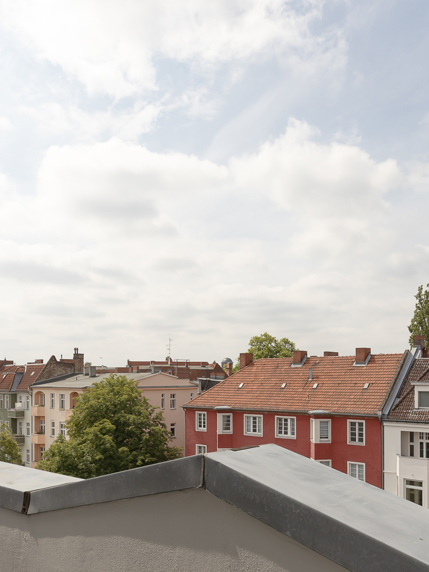Blick von einem Balkon auf bunte Wohnhäuser mit roten Dächern und Bäumen.