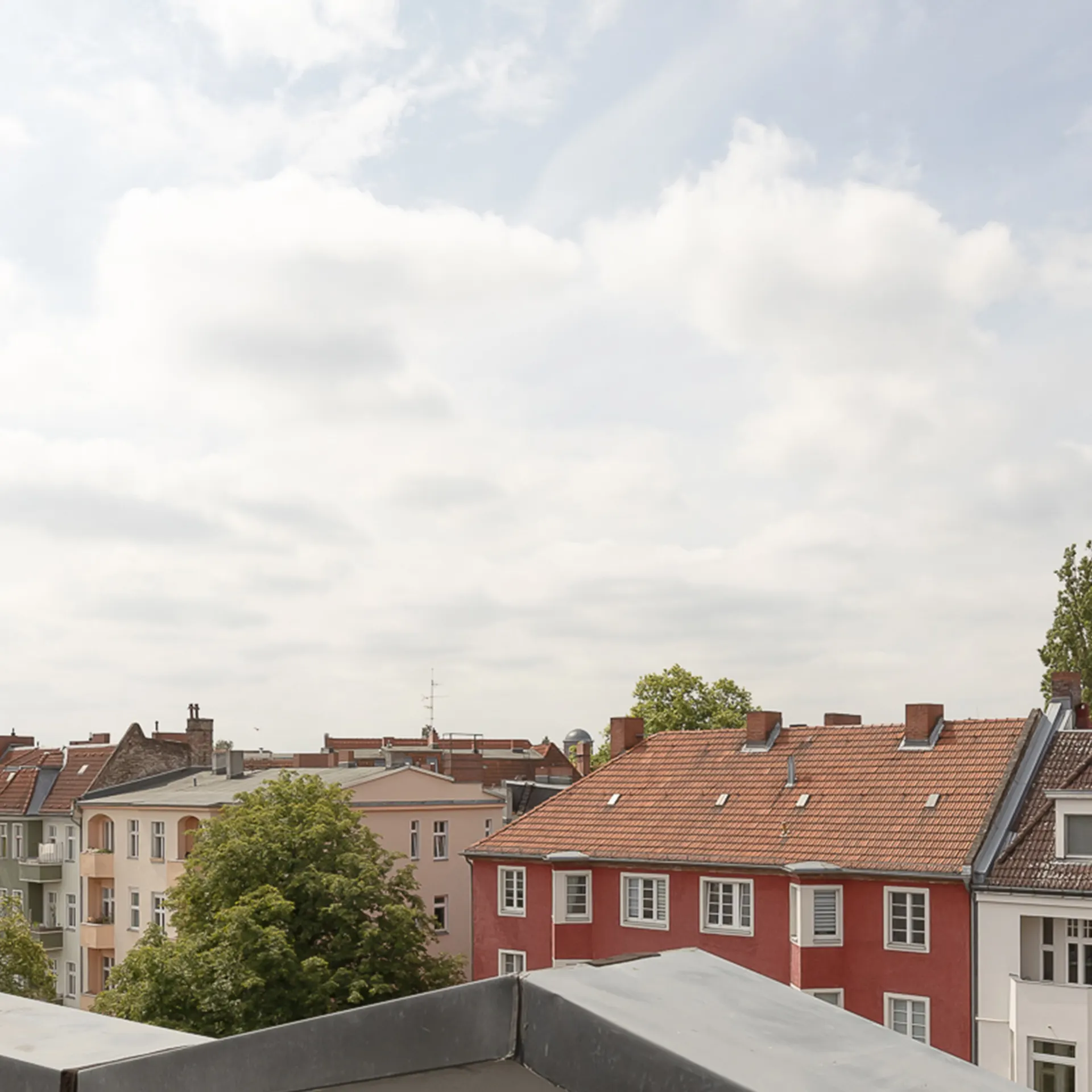 Blick von einem Balkon auf bunte Wohnhäuser mit roten Dächern und Bäumen.