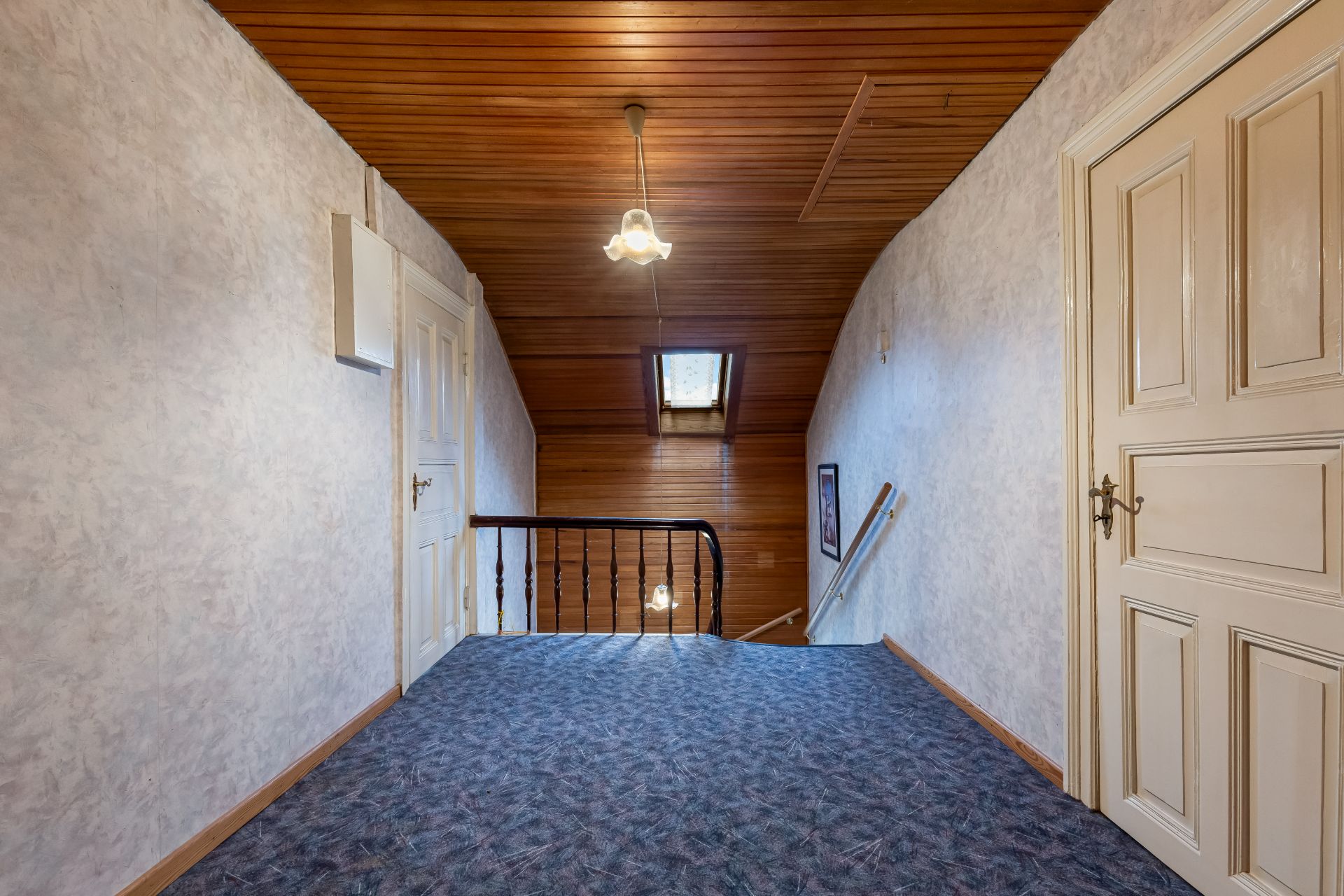Flur mit Teppichboden, Holzdecke, zwei Türen und Treppe mit Geländer.