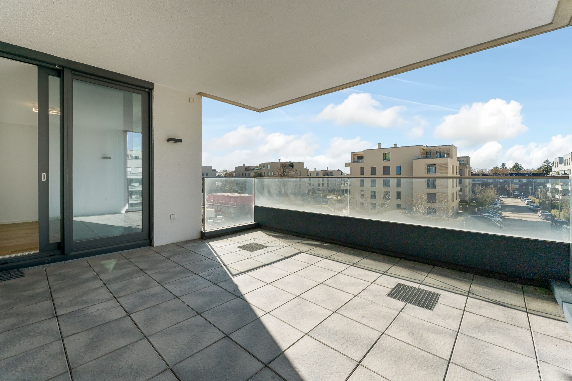 Großer Balkon mit Glasgeländer und Blick auf umliegende Wohngebäude.