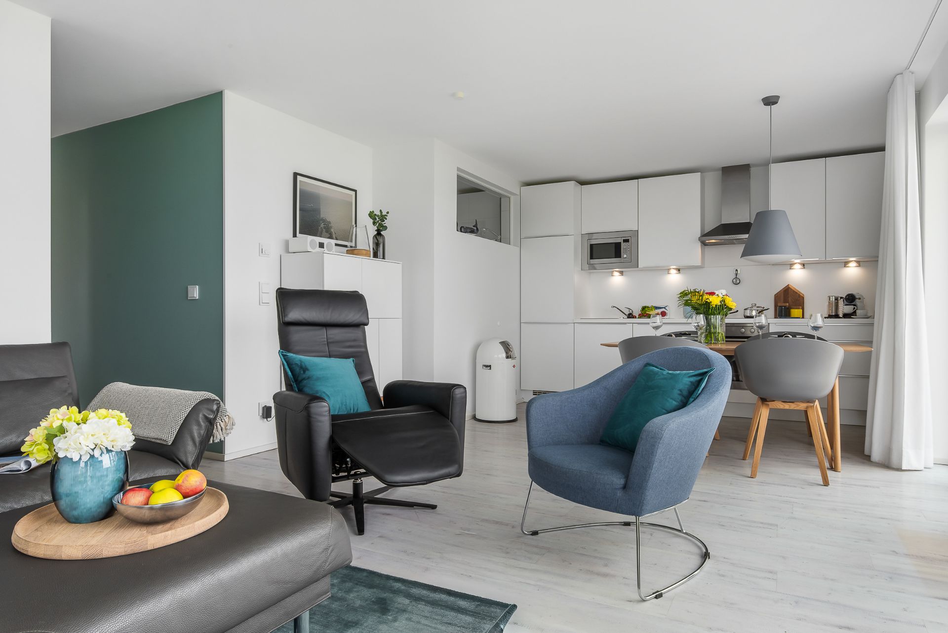 Modernes Wohnzimmer mit Sesseln, Couch, Esstisch und offener Küche.