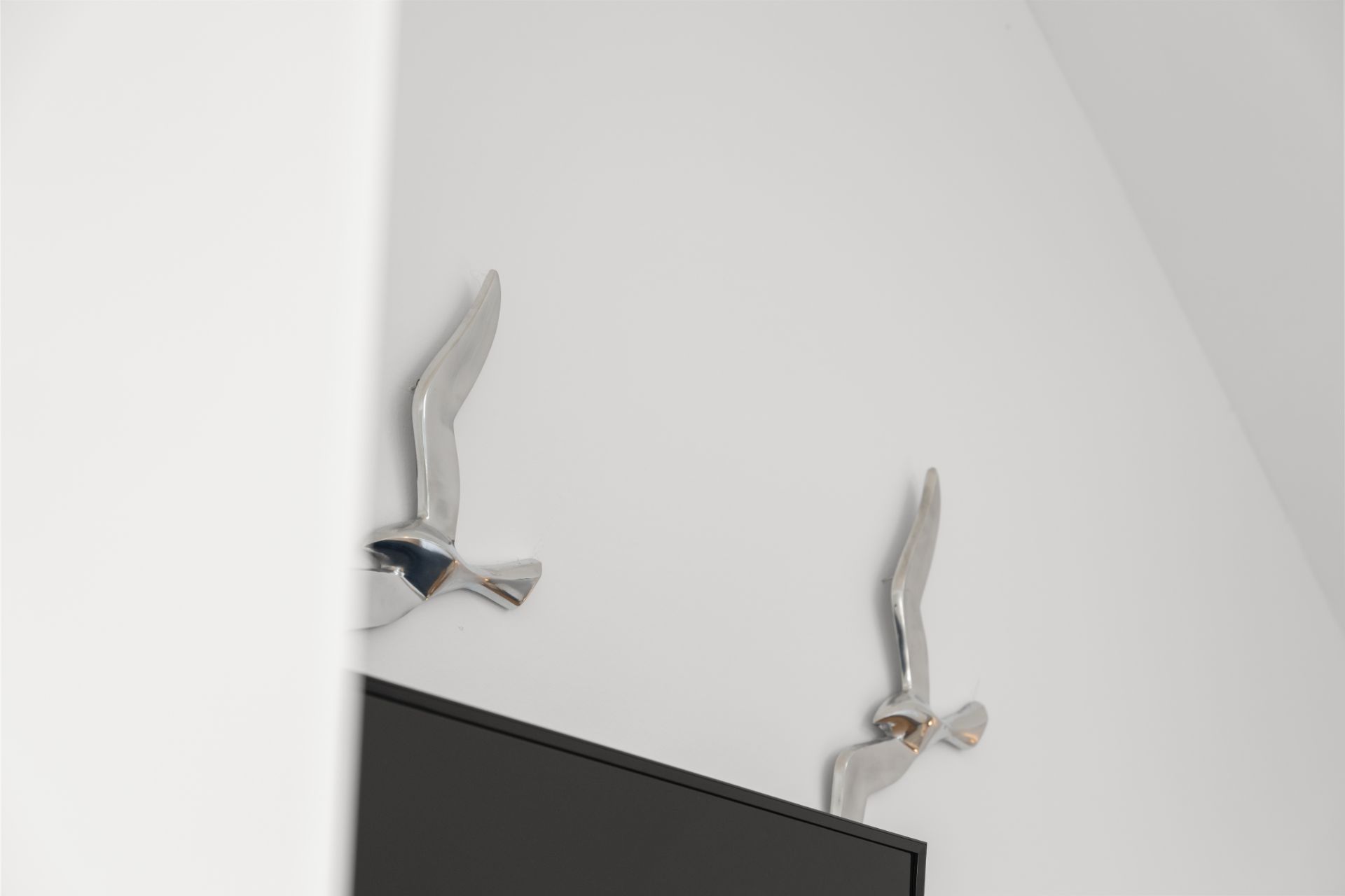 Zwei silberne Möwen-Dekorationen an einer weißen Wand über einem schwarzen Fernseher.