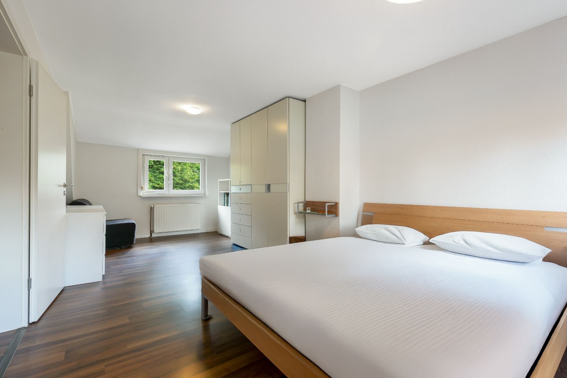 Helles Schlafzimmer mit Doppelbett, Kleiderschrank und Fenster mit Blick ins Grüne.