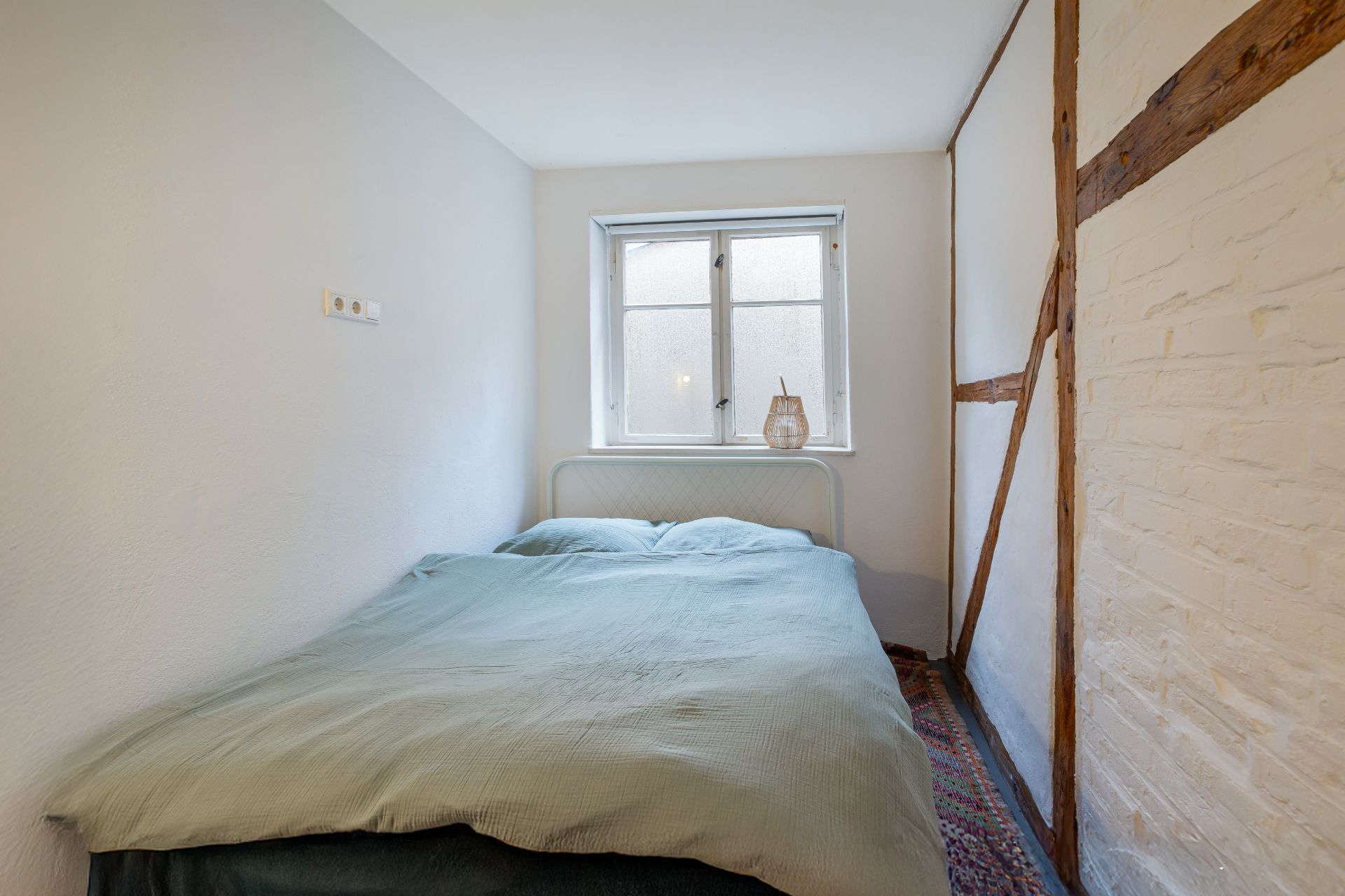 Kleines Schlafzimmer mit Doppelbett, Fenster und Nachttisch mit Lampe.