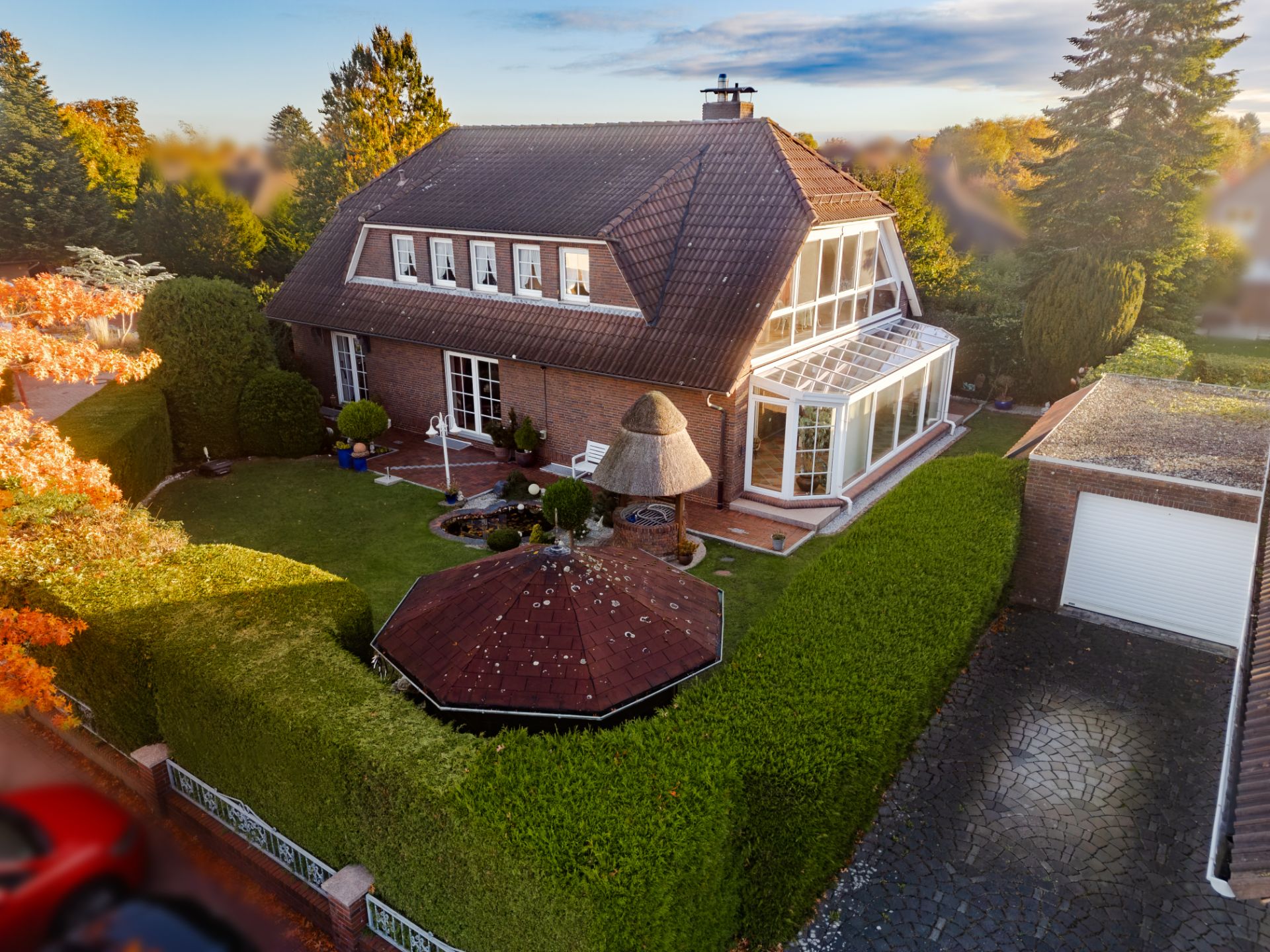 Backsteinhaus mit Wintergarten, gepflegtem Garten, Pavillon und Garage bei Sonnenuntergang.