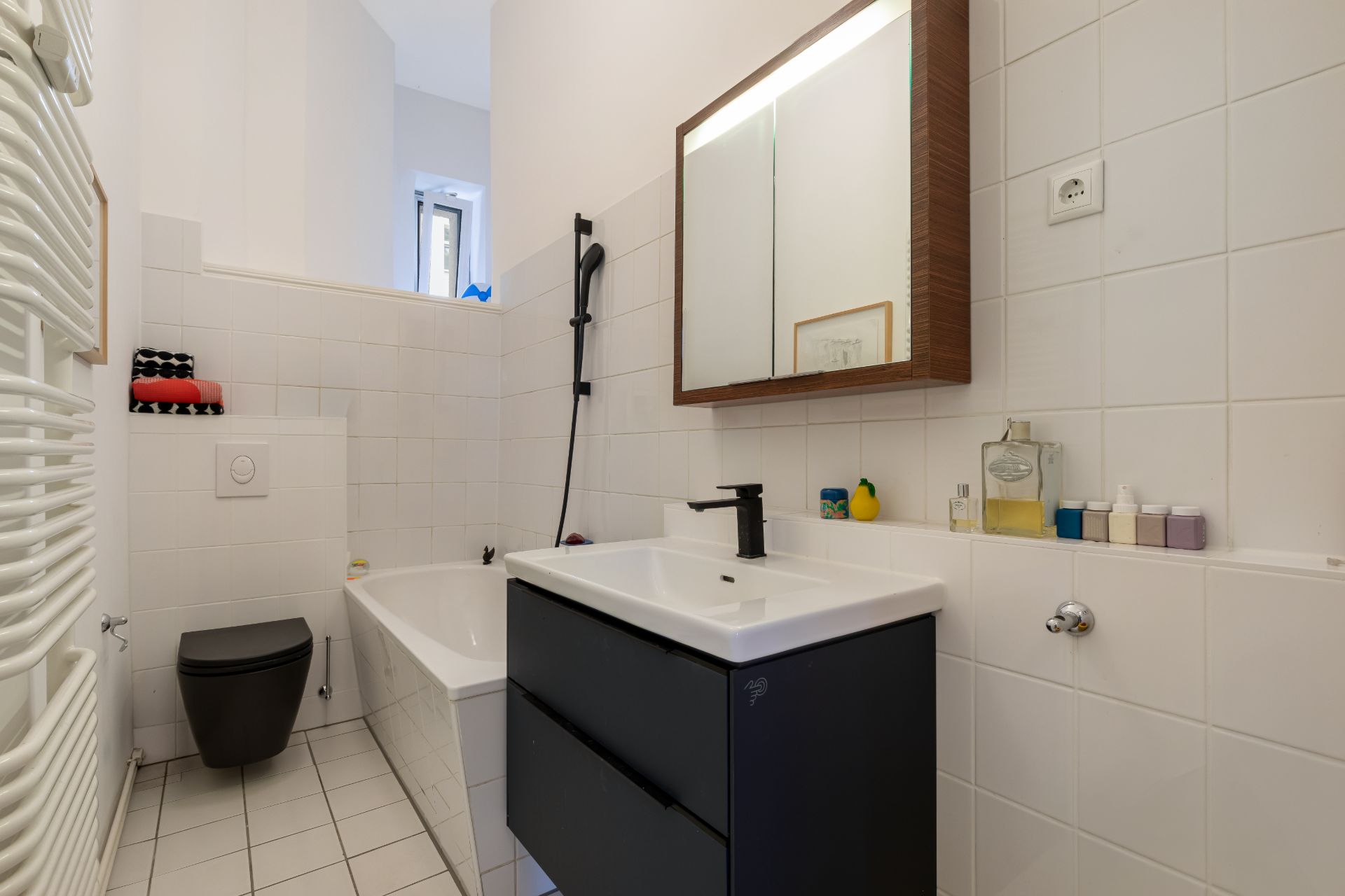 Modernes Badezimmer mit Badewanne, Waschbecken, schwarzem WC und großem Spiegel.