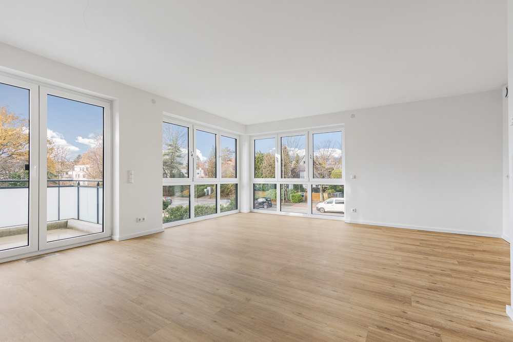 Helles, leeres Zimmer mit Parkettboden und großen Fenstern, Blick auf den Balkon und Straße.