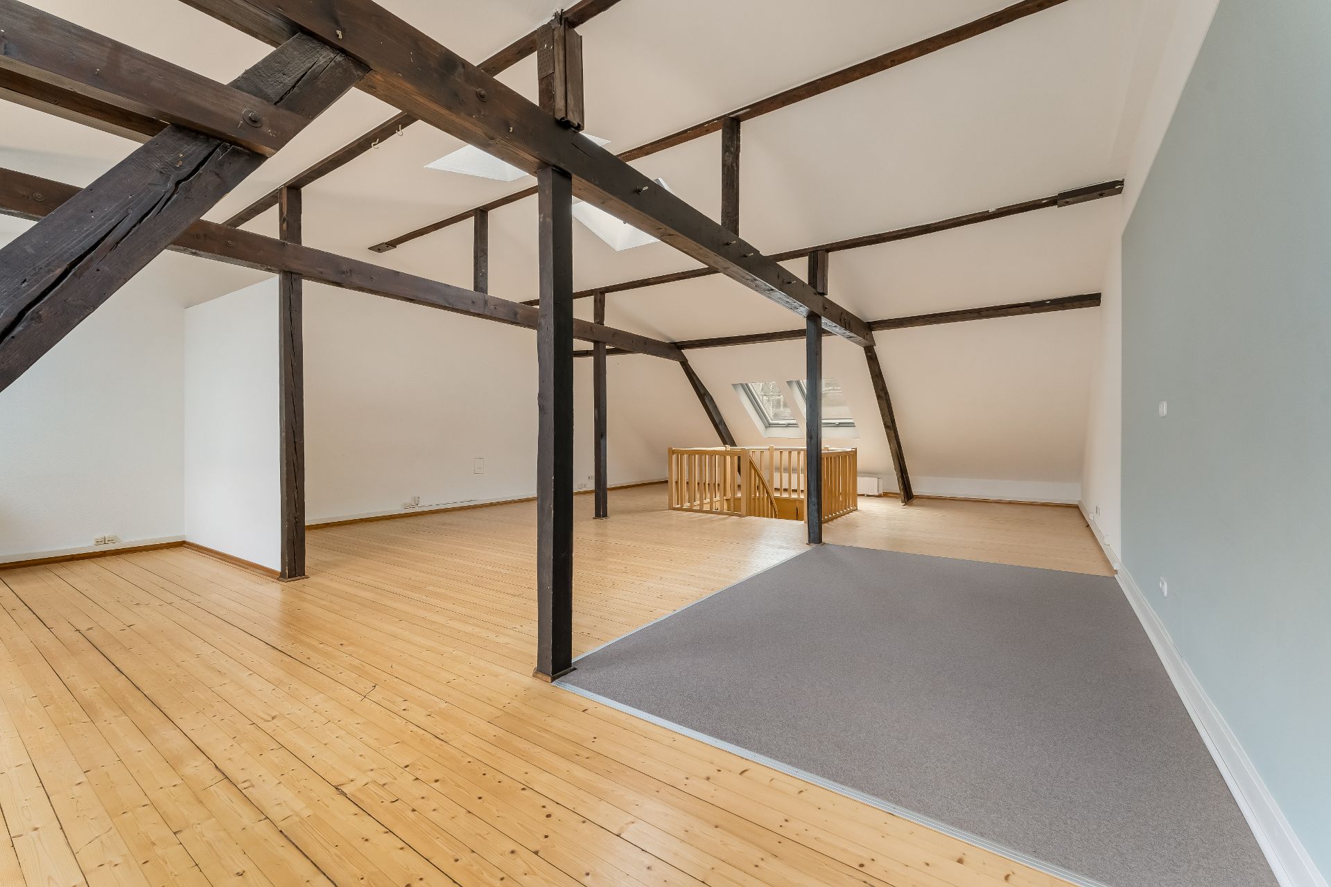 Heller Dachbodenraum mit Holzbalken, Holzfußboden und einer abgetrennten Teppichfläche.