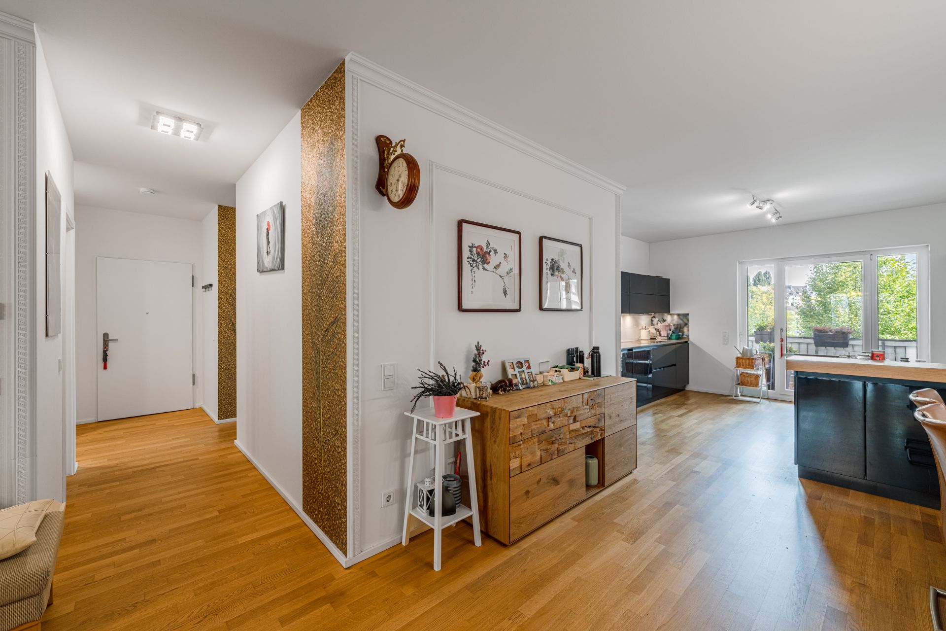 Wohnungsflur mit Holzboden, Kommode, Wanddeko und Blick auf Küche und Balkon.