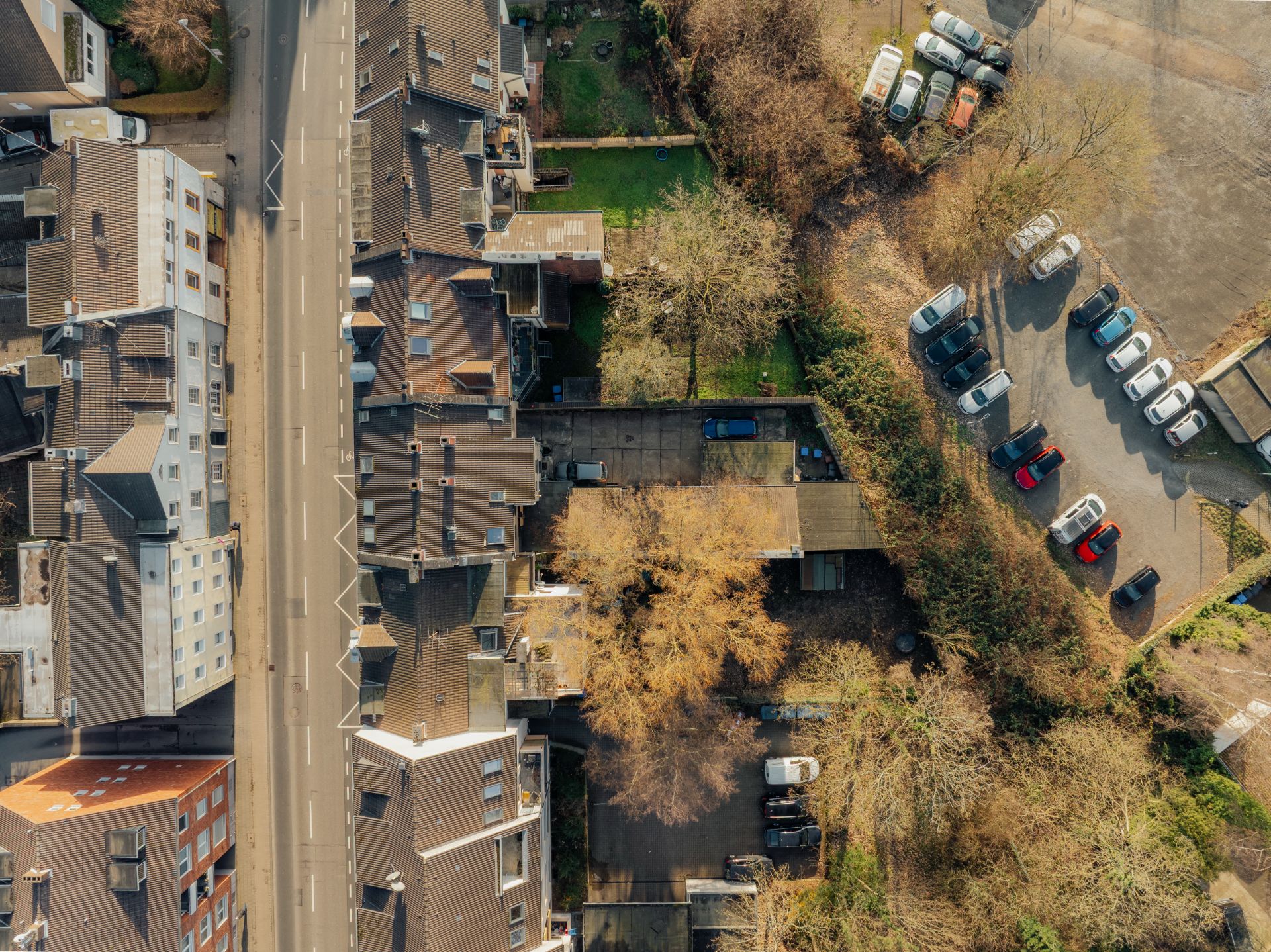 Luftaufnahme von Wohnhäusern, einer Straße und einem Parkplatz mit mehreren Autos.