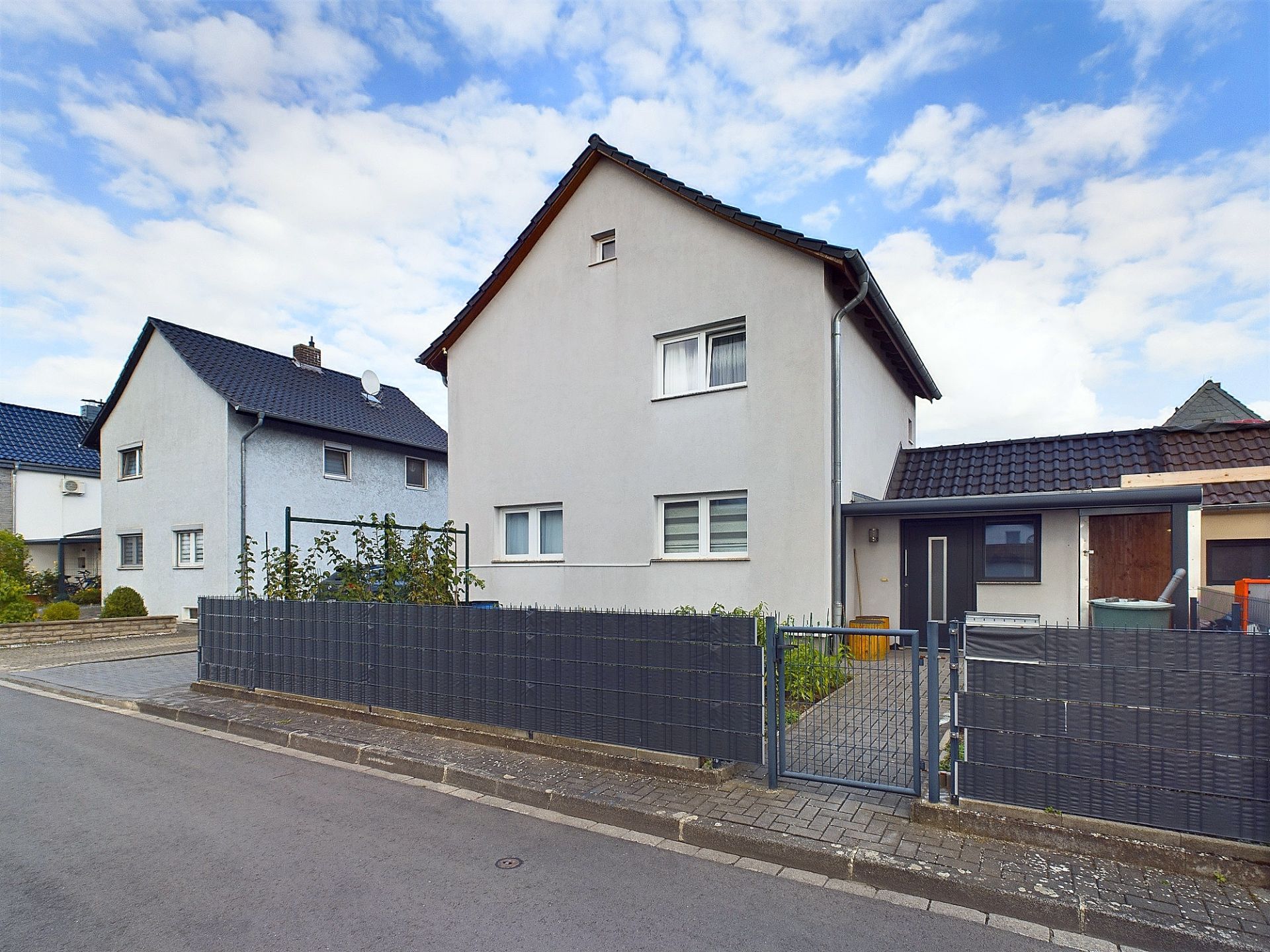 Zweistöckiges Wohnhaus mit eingezäuntem Vorgarten und gepflastertem Weg zur Haustür.