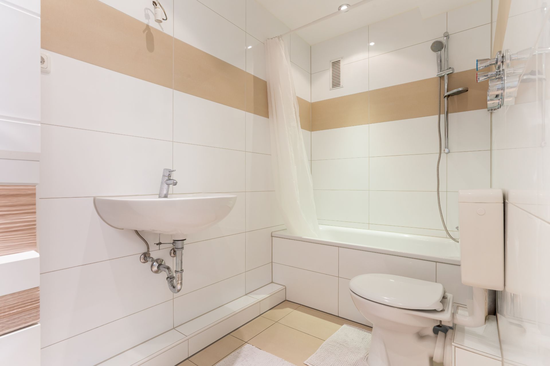 Modernes Bad mit weißem Waschbecken, Toilette, Badewanne und Dusche, hell gefliest.