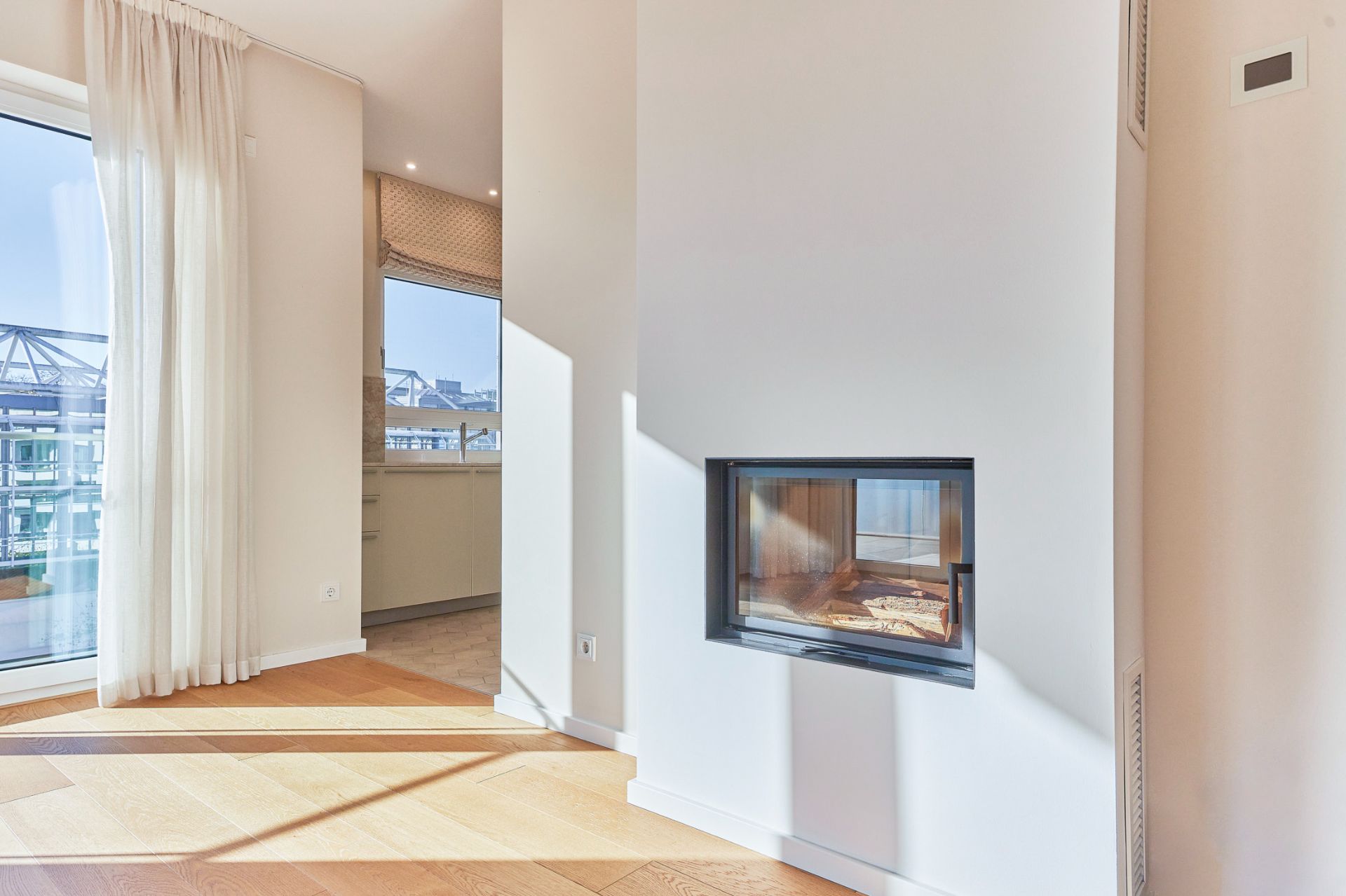Helles Wohnzimmer mit Kamin, Parkettboden und großen Fenstern mit Vorhängen.