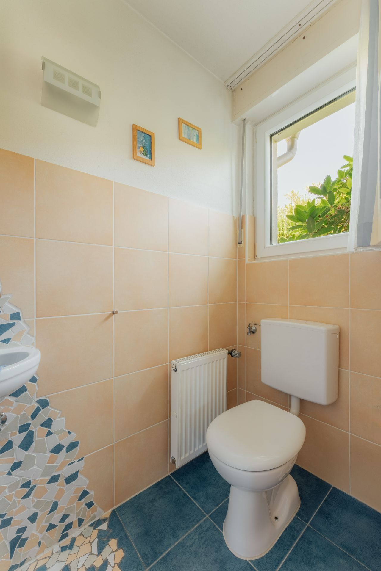 Kleines Badezimmer mit Toilette, Waschbecken, Fenster und Wandbildern.