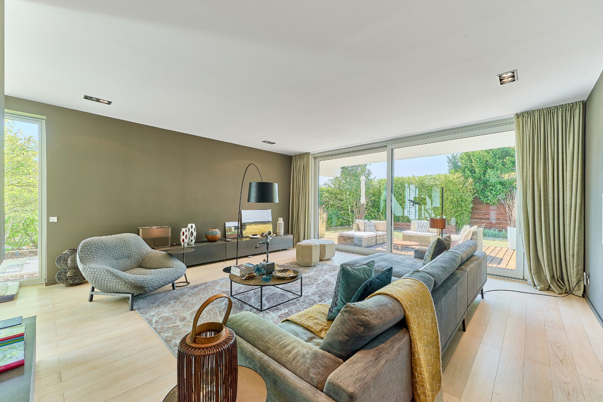 Modernes Wohnzimmer mit Sofa, Sessel, Couchtisch und großer Fensterfront zum Garten.