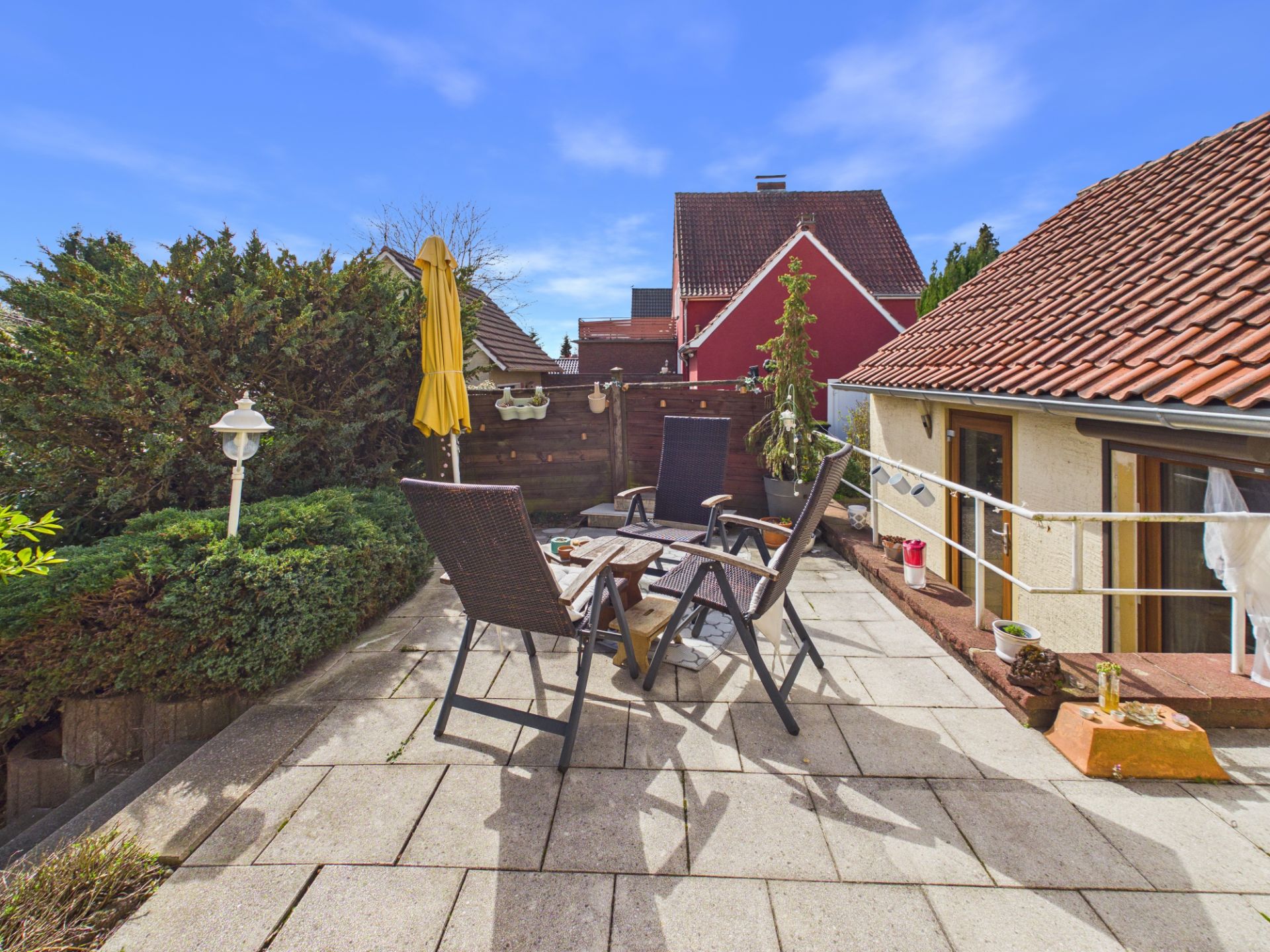 Terrasse mit Tisch, vier Stühlen, gelbem Sonnenschirm und umgeben von Pflanzen.