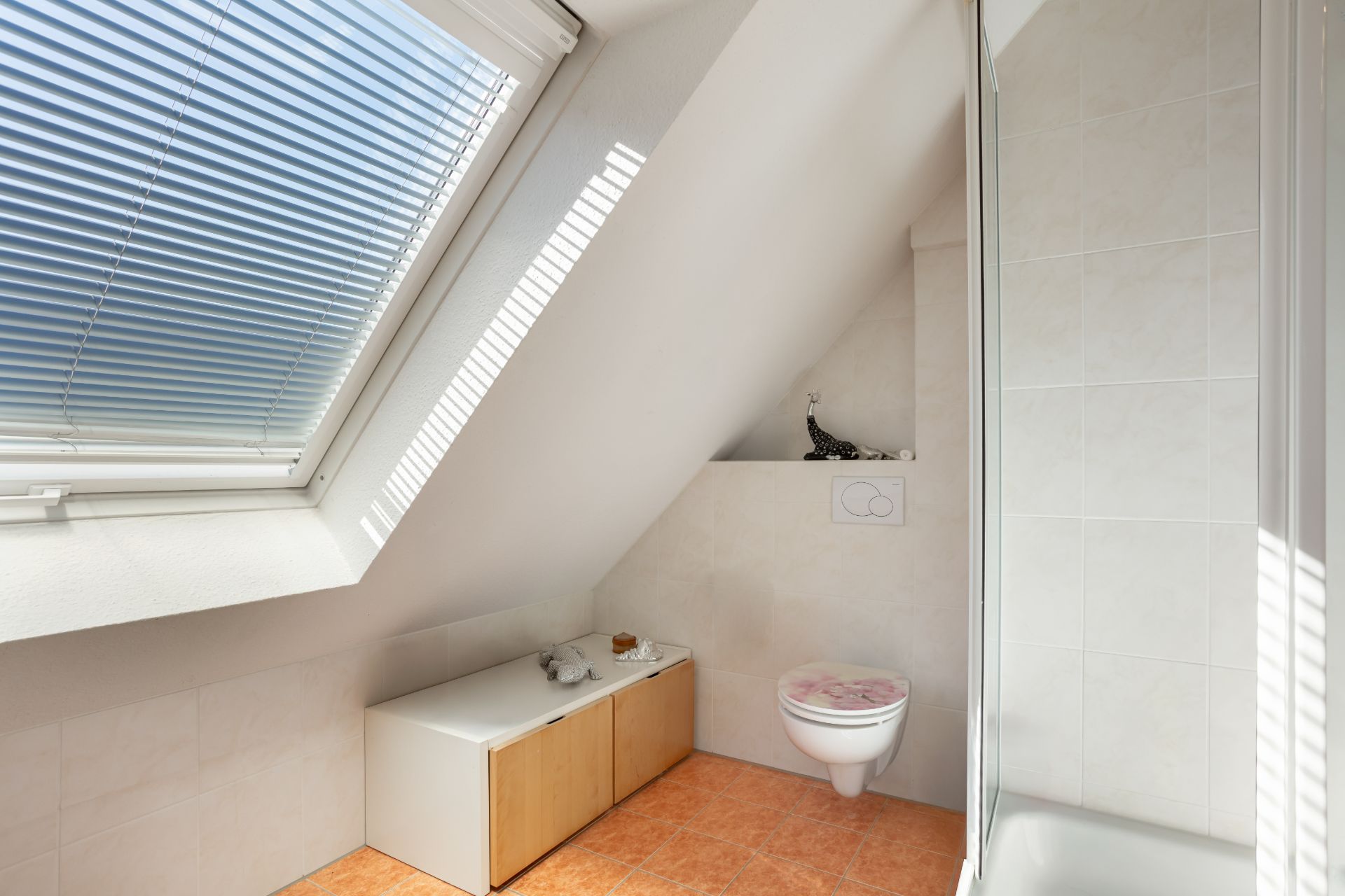 Badezimmer mit Dachfenster, WC, Duschkabine und niedrigem Schrank auf orangefarbenen Fliesen.