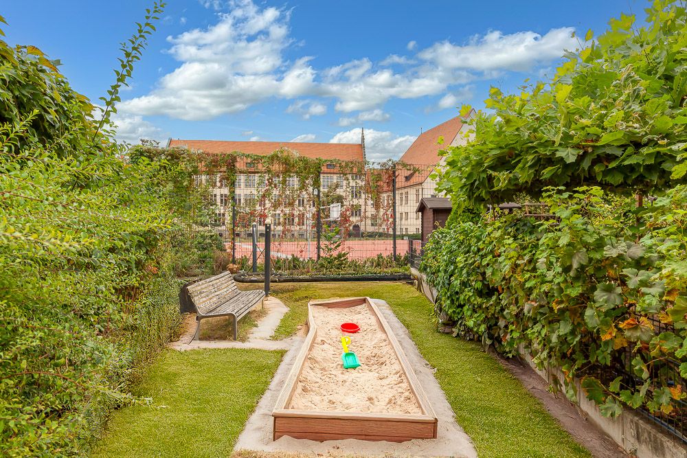 Sandkasten mit Spielzeug im Garten, daneben eine Holzbank und viel Grün.