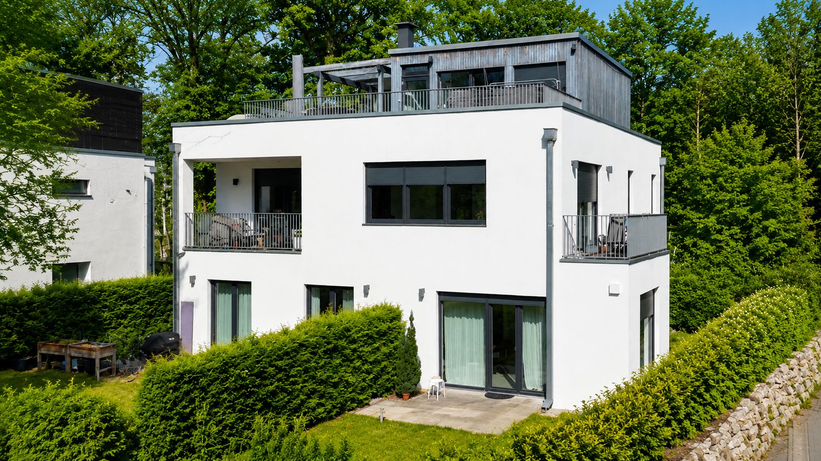 Modernes weißes Wohnhaus mit Flachdach, mehreren Balkonen und umliegendem Garten.