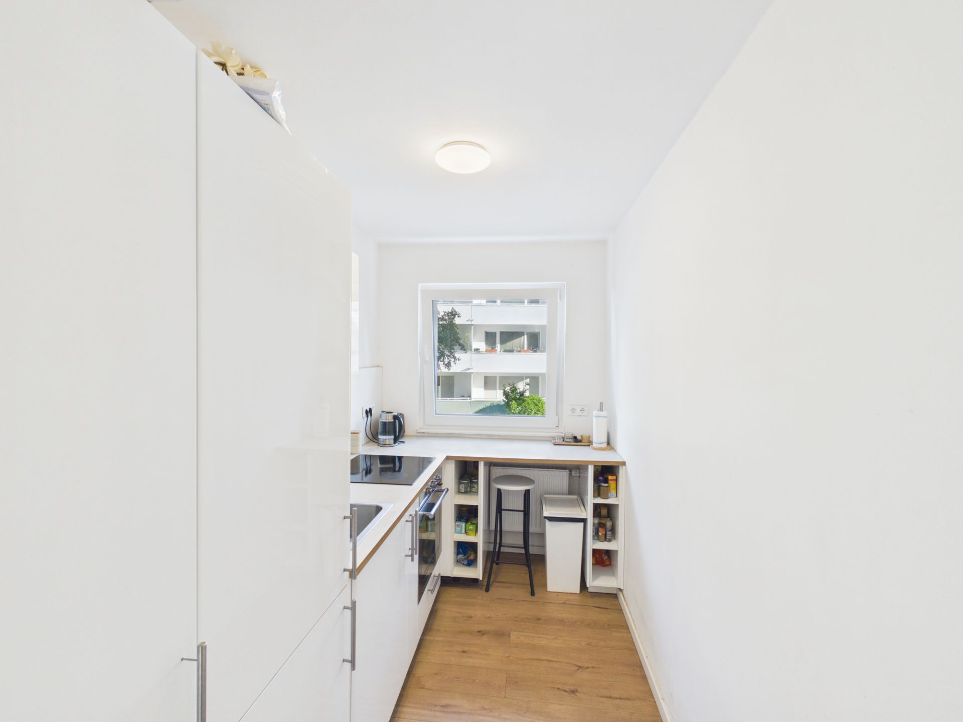 Helle, schmale Küche mit Fenster, weißen Möbeln und Holzfußboden.