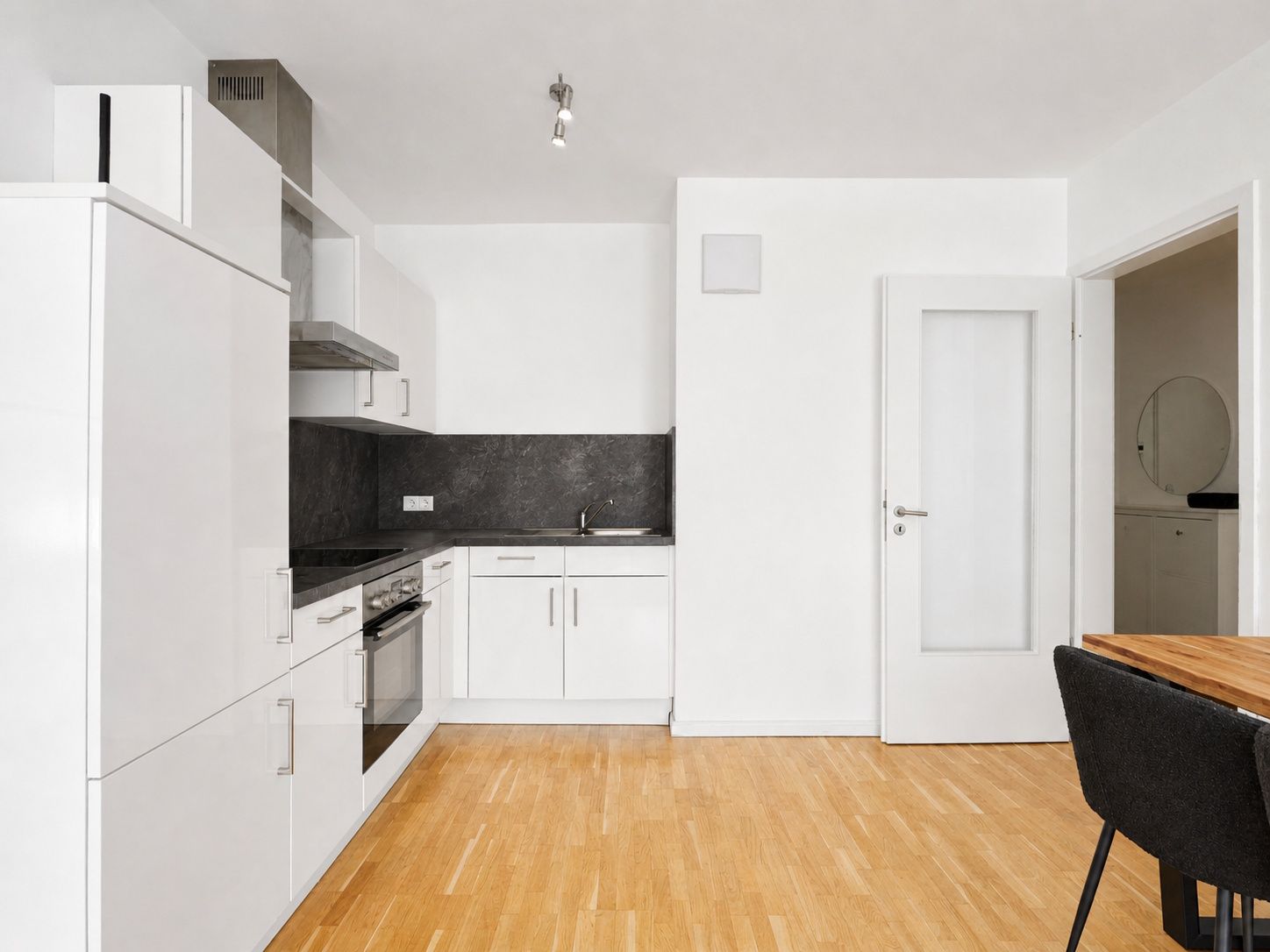 Moderne weiße Einbauküche mit Holzfußboden und Esstisch in einem hellen Raum.
