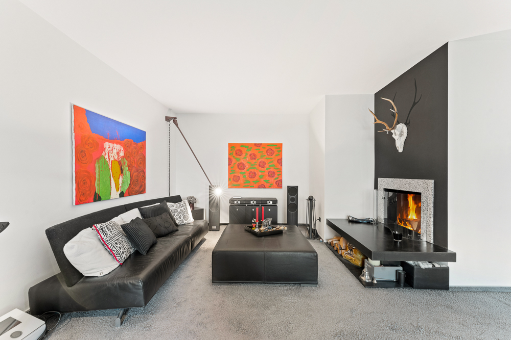 Modernes Wohnzimmer mit schwarzem Sofa, Kunst an den Wänden und Kamin mit Feuer.