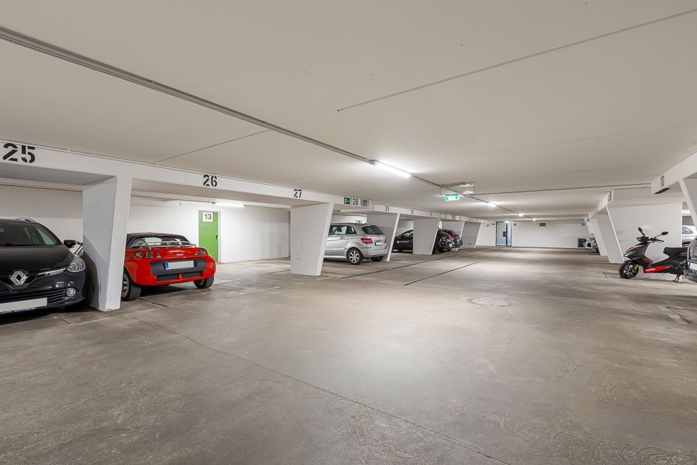 Tiefgarage mit mehreren Autos und Motorrädern auf markierten Parkplätzen.