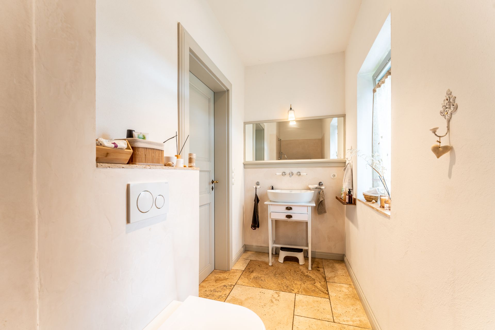 Helles Badezimmer mit Waschbecken, Spiegel, Fenster und Dekoration auf Ablagen.