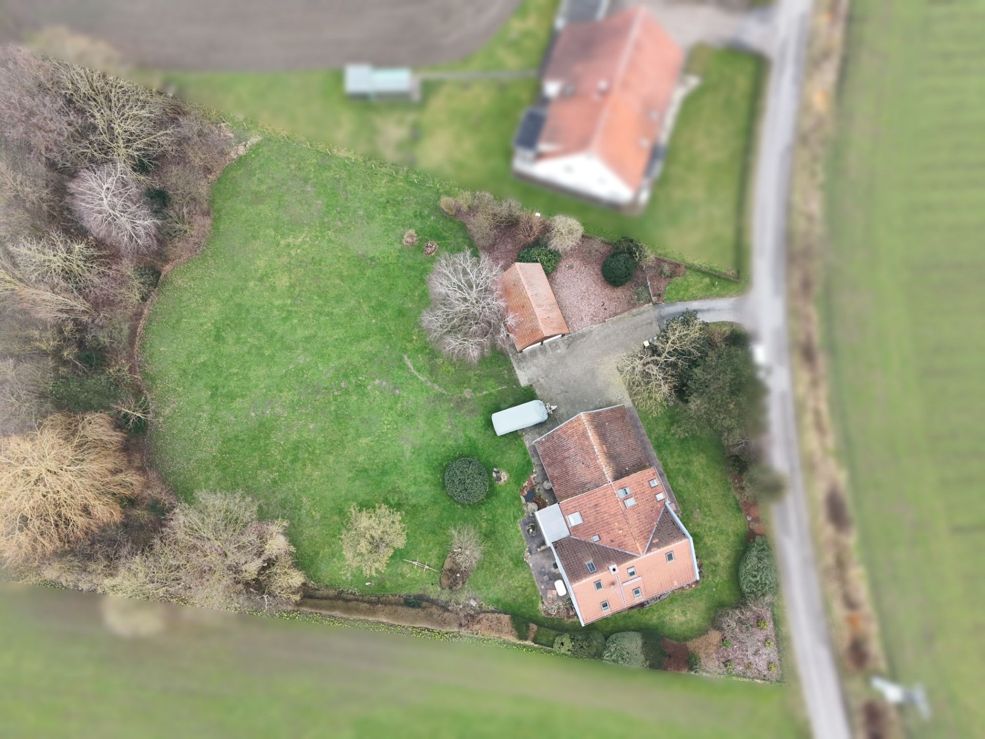 Luftaufnahme eines Hauses mit rotem Dach, großem Garten und Bäumen.