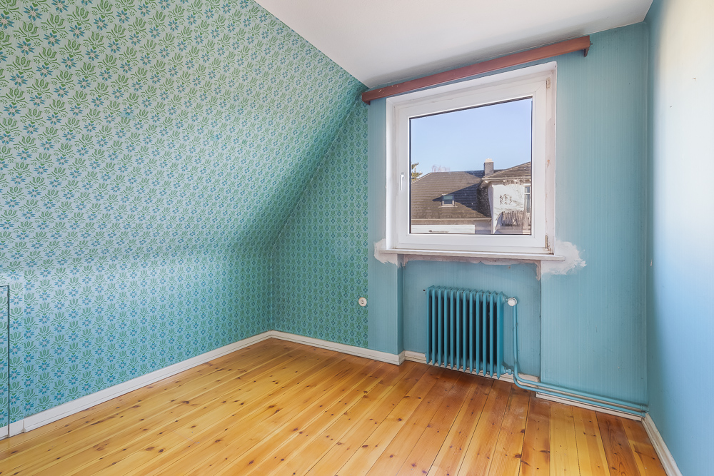 Leeres Zimmer mit gemusterten blauen Wänden, Holzfußboden, Fenster und Heizkörper.