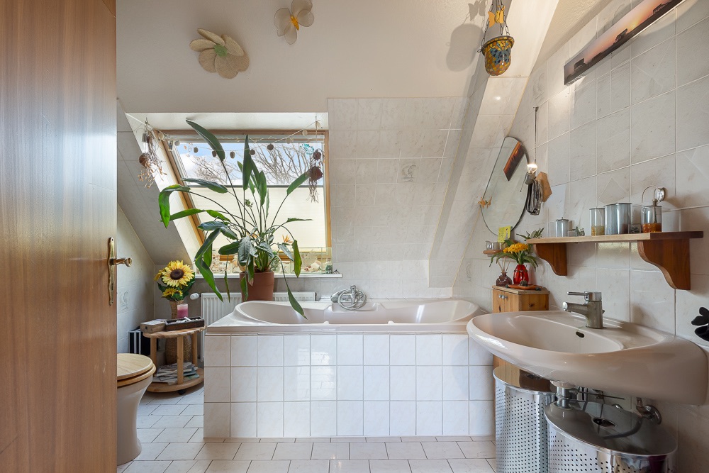 Helles Badezimmer mit Badewanne, Waschbecken, Pflanzen und Fenster unter einer Dachschräge.