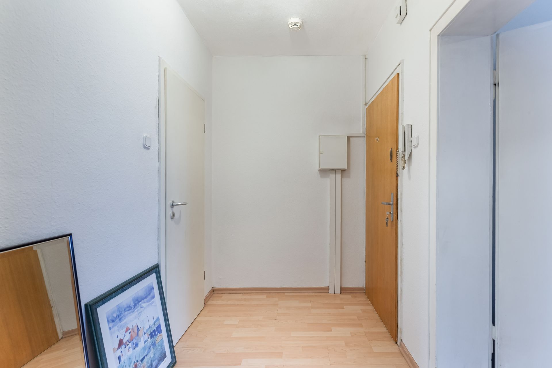 Flur mit Holzboden, weiß gestrichenen Wänden und zwei Bildern, die an die Wand gelehnt sind.