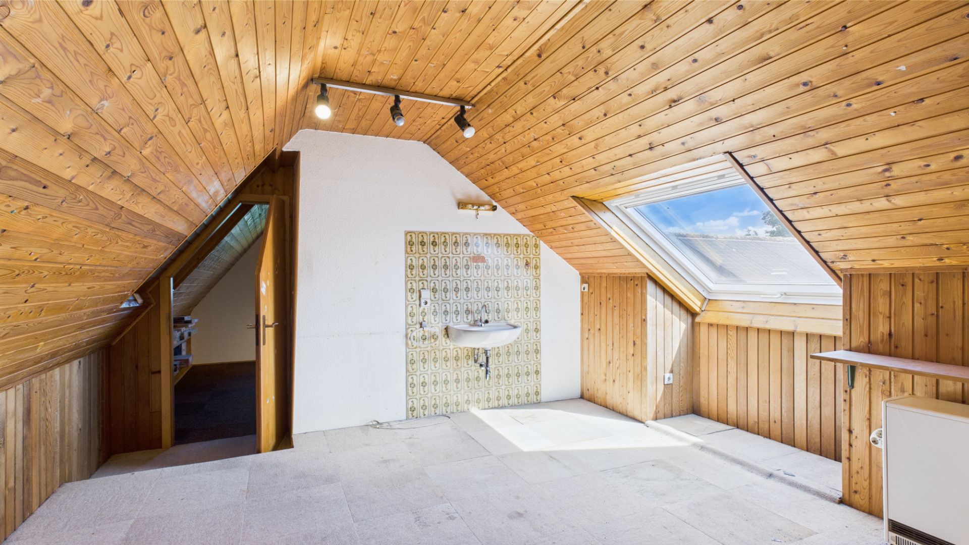 Dachzimmer mit Holzverkleidung, Dachfenster und Waschbecken an der Wand.