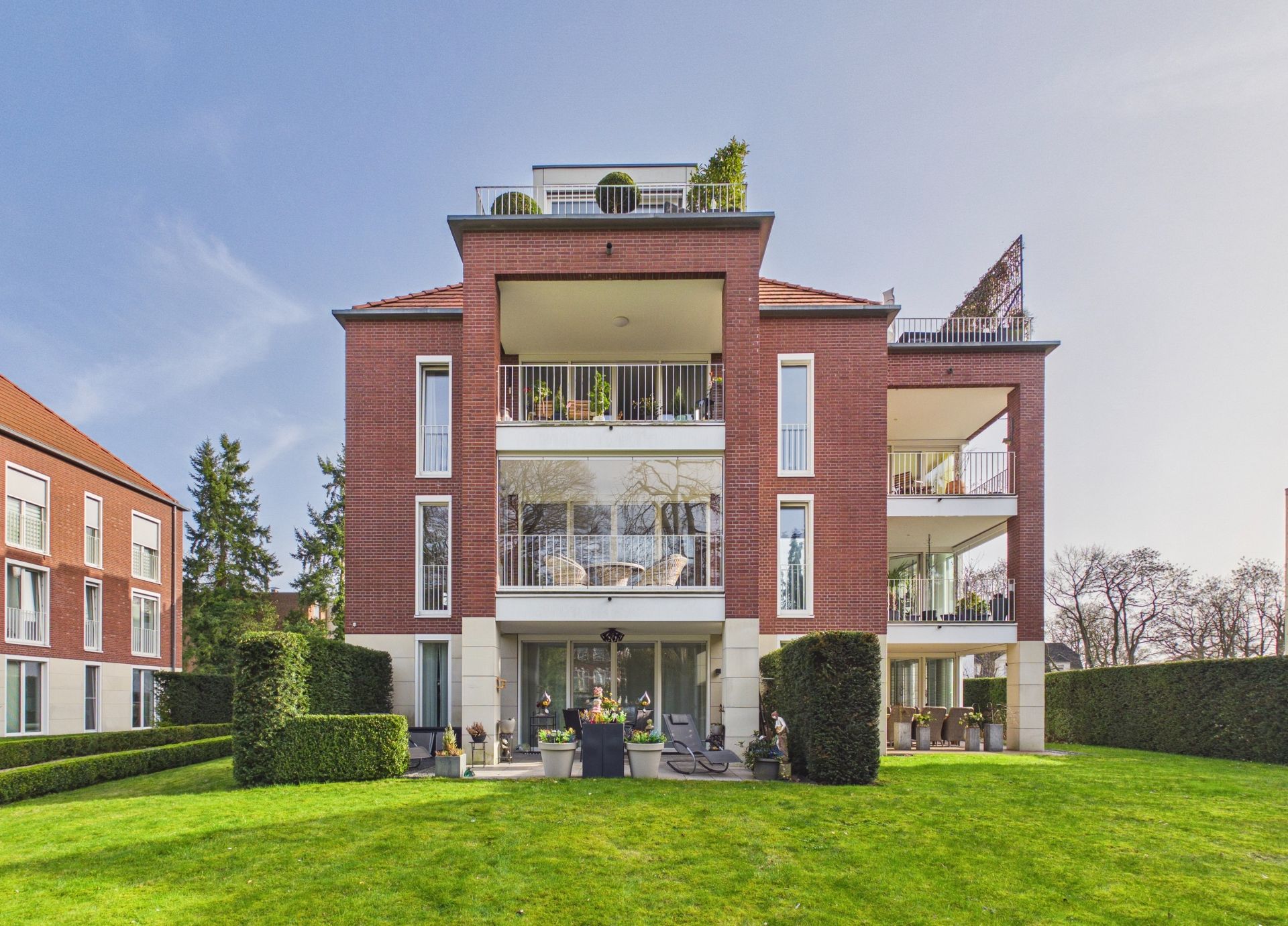 Modernes Mehrfamilienhaus mit Balkonen und großem Garten, rote Backsteinfassade, klare Fenster.