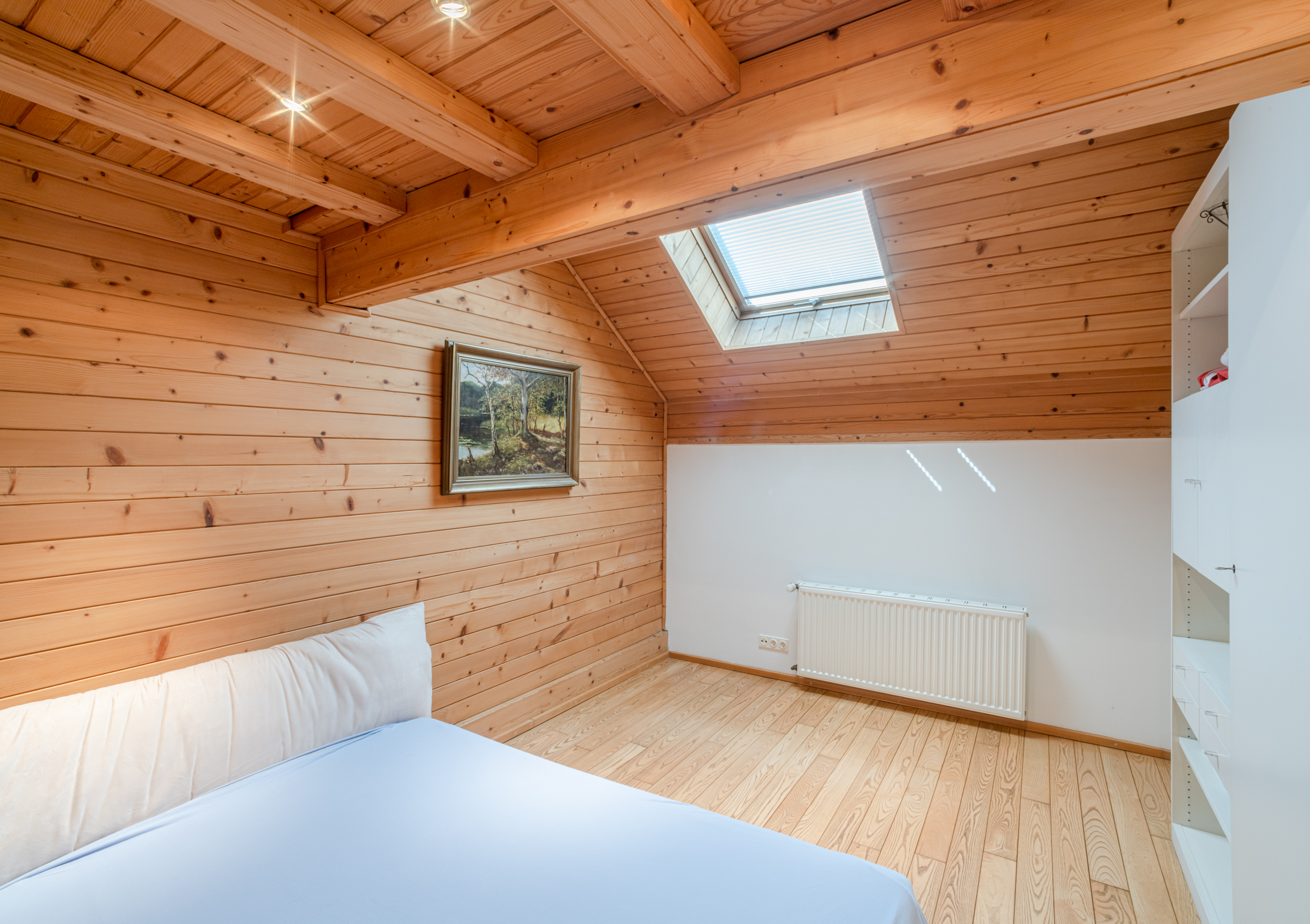 Helles Schlafzimmer mit Holzverkleidung, Dachfenster, Bett und Regal.