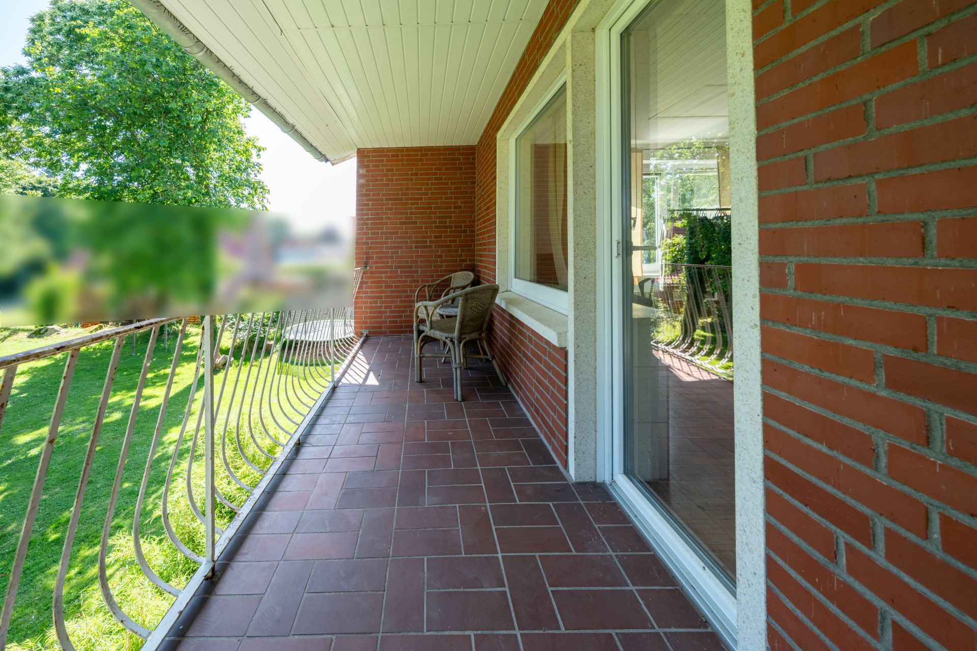 Überdachter Balkon mit Terrakottafliesen, zwei Stühlen und Blick auf den Garten.
