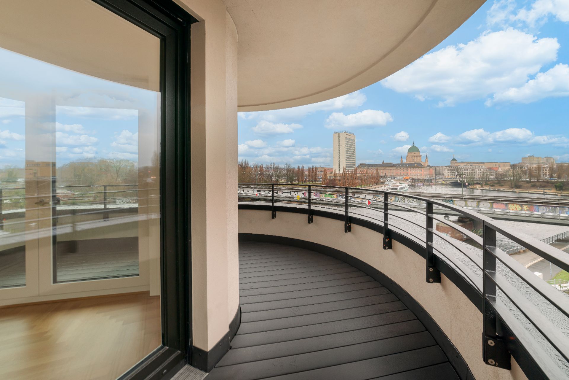 Halbrunder Balkon mit Glasgeländer und Blick auf Stadt und Fluss.
