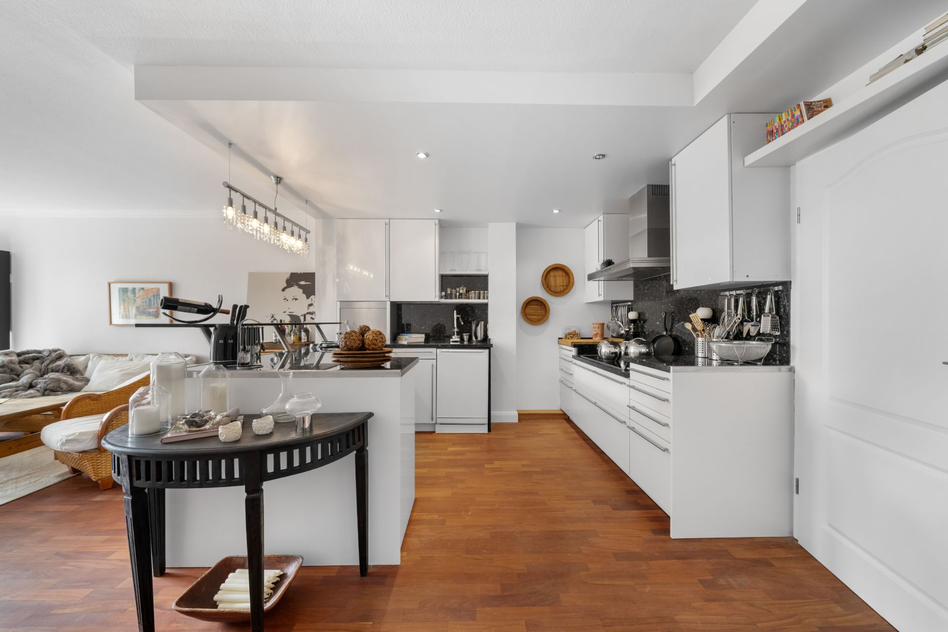 Moderne, weiße Einbauküche mit Holzboden und Essbereich, Blick ins Wohnzimmer.