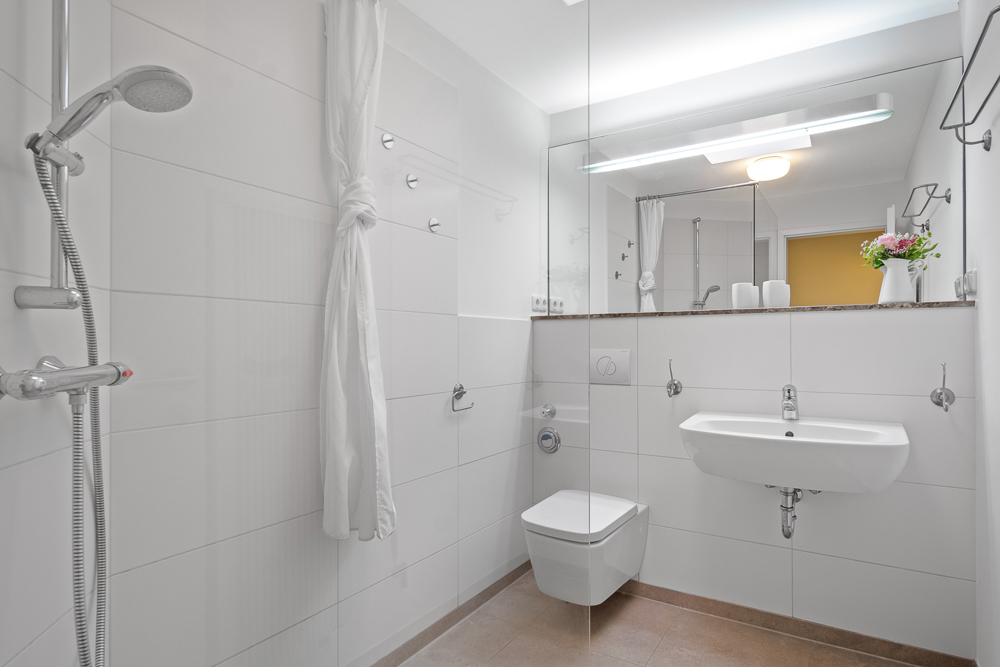 Modernes Bad mit Dusche, WC, Waschbecken, Spiegel und weißen Fliesen.