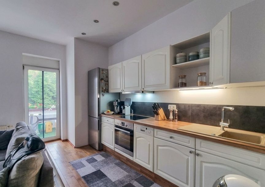 Moderne Wohnküche mit weißen Schränken, Elektrogeräten, Sofa und Zugang zum Balkon.