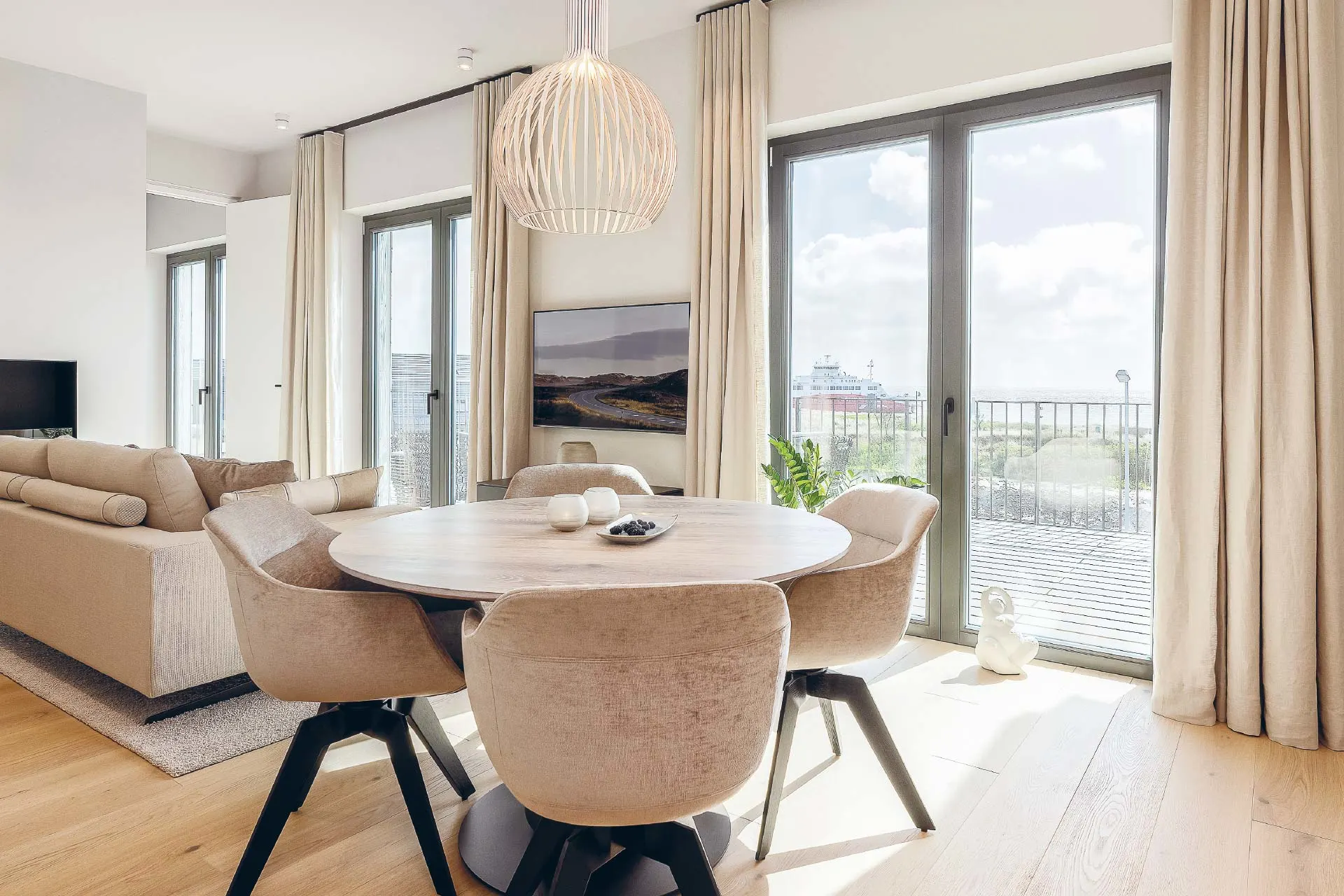 Helles Wohnzimmer mit Esstisch, fünf Stühlen und großen Fenstern zur Terrasse.