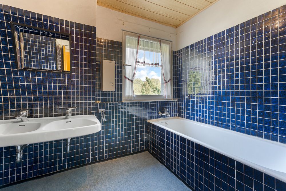 Badezimmer mit blauen Fliesen, Doppelwaschbecken, Badewanne und Fenster mit Vorhang.