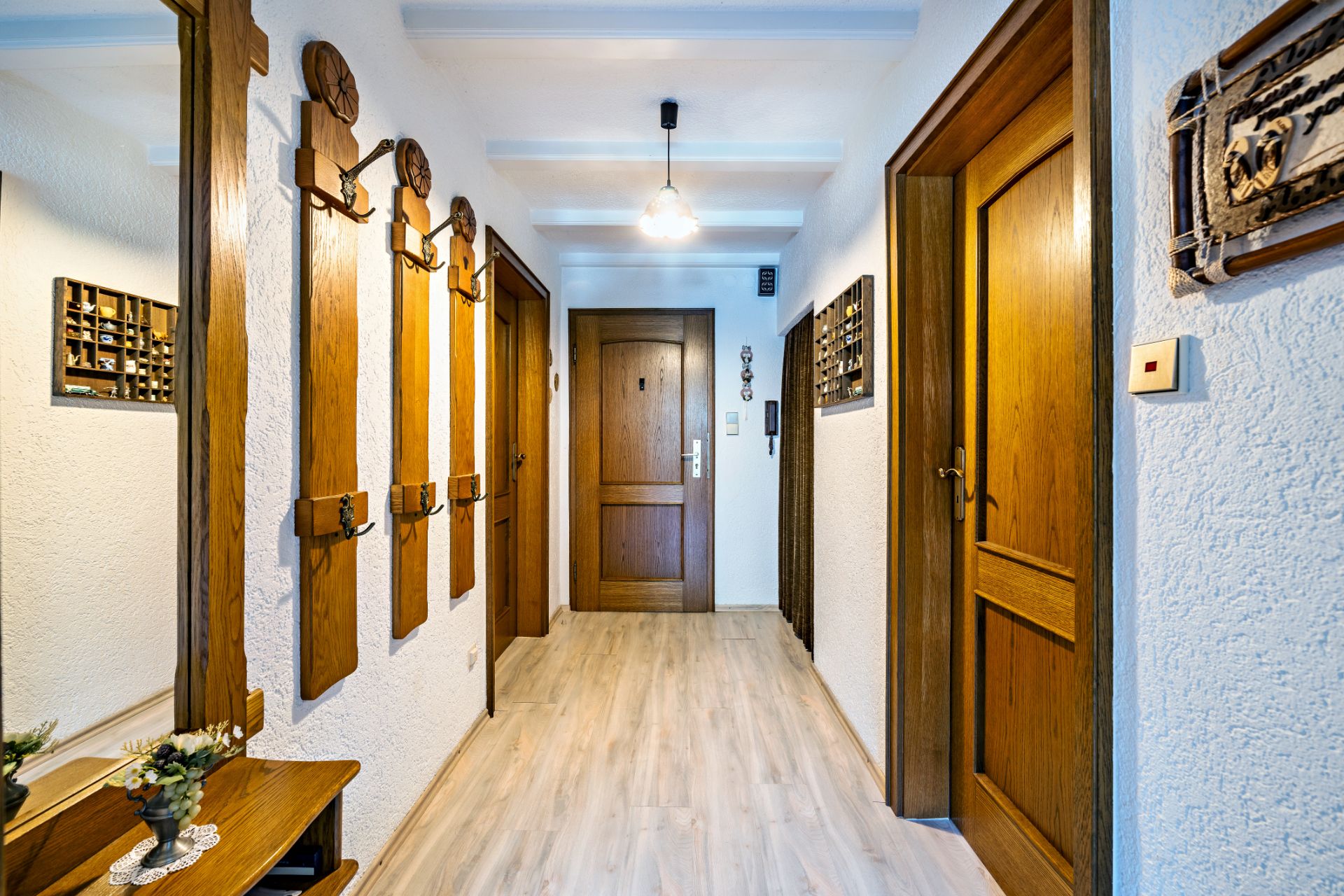 Heller Flur mit Holztüren, Garderobe aus Holz und einem kleinen Tisch mit Blumenvase.
