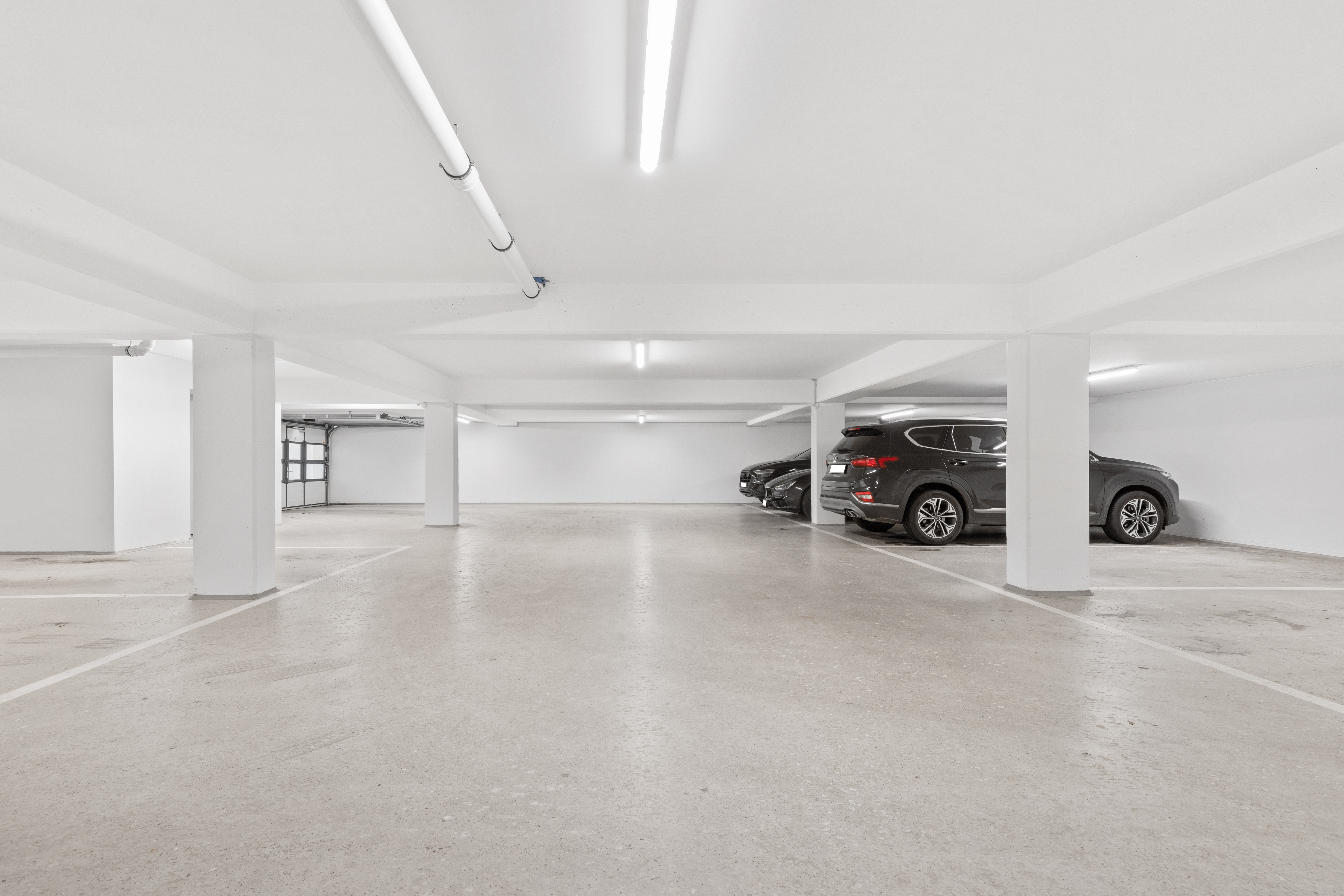 Helle Tiefgarage mit parkenden Autos und freien Stellplätzen, weiße Wände und Säulen.