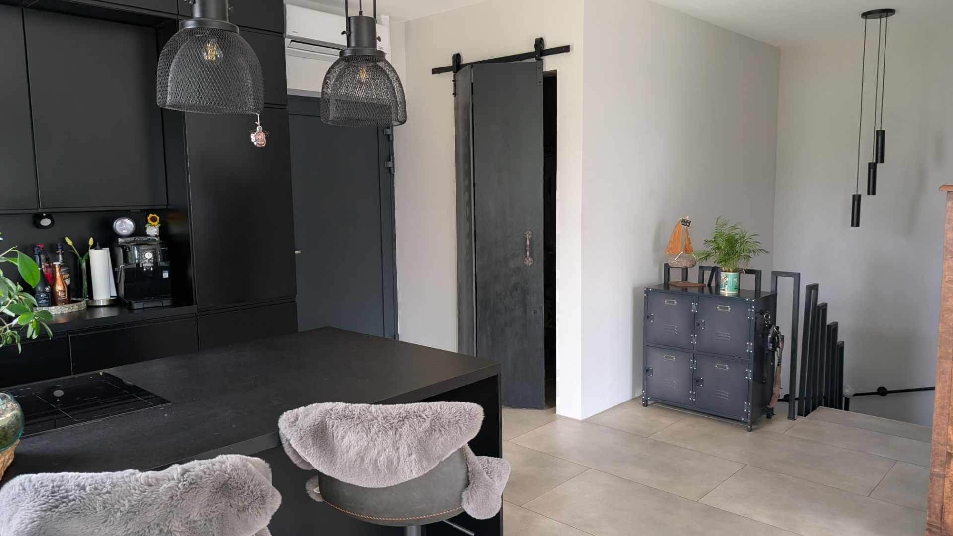 Moderne Küche mit schwarzer Einrichtung, Bartheke und Hockern, daneben Flur mit Sideboard und Treppenabgang.