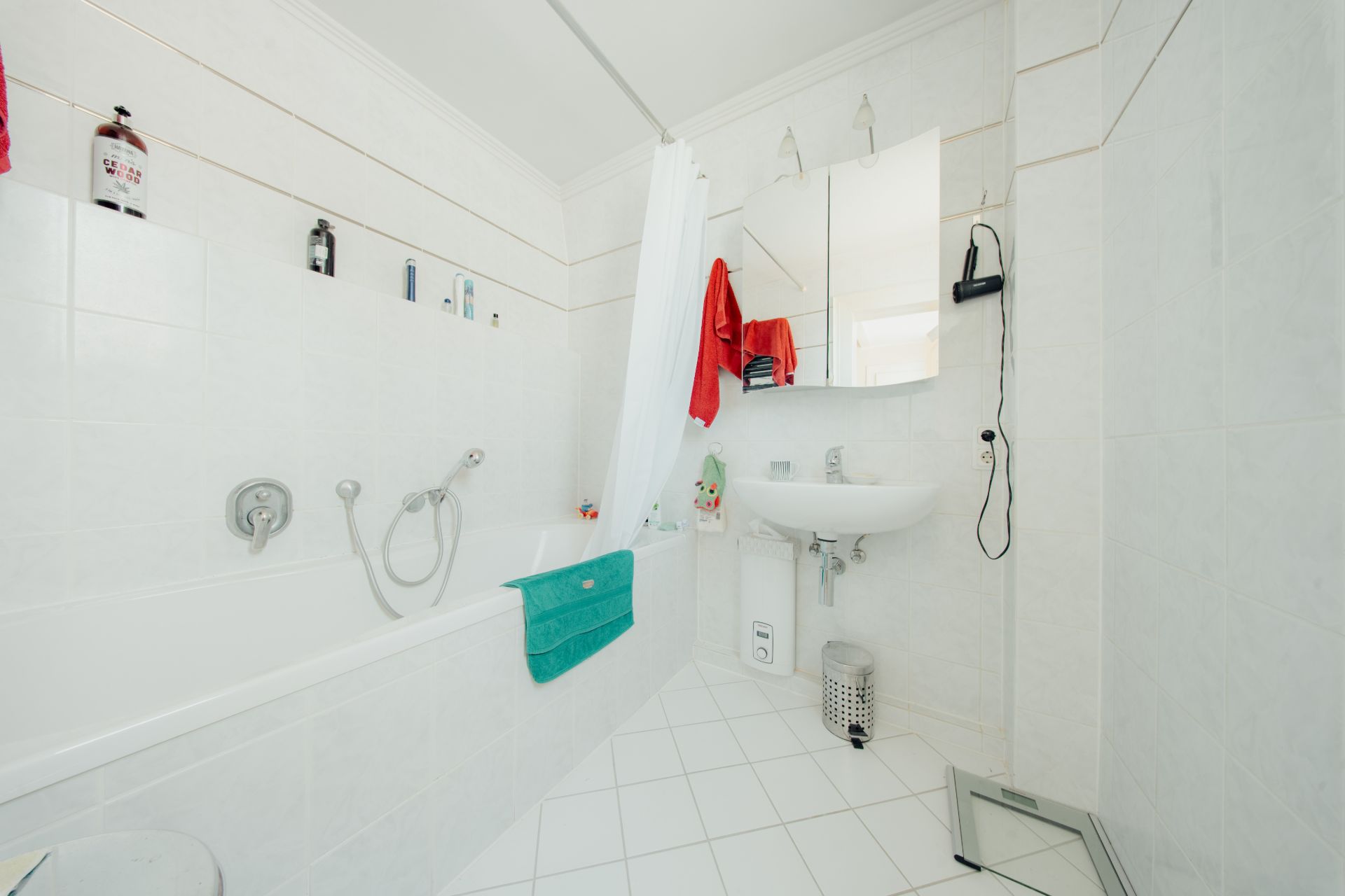 Helles Badezimmer mit Badewanne, Duschvorhang, Waschbecken, Spiegel und weißen Fliesen.