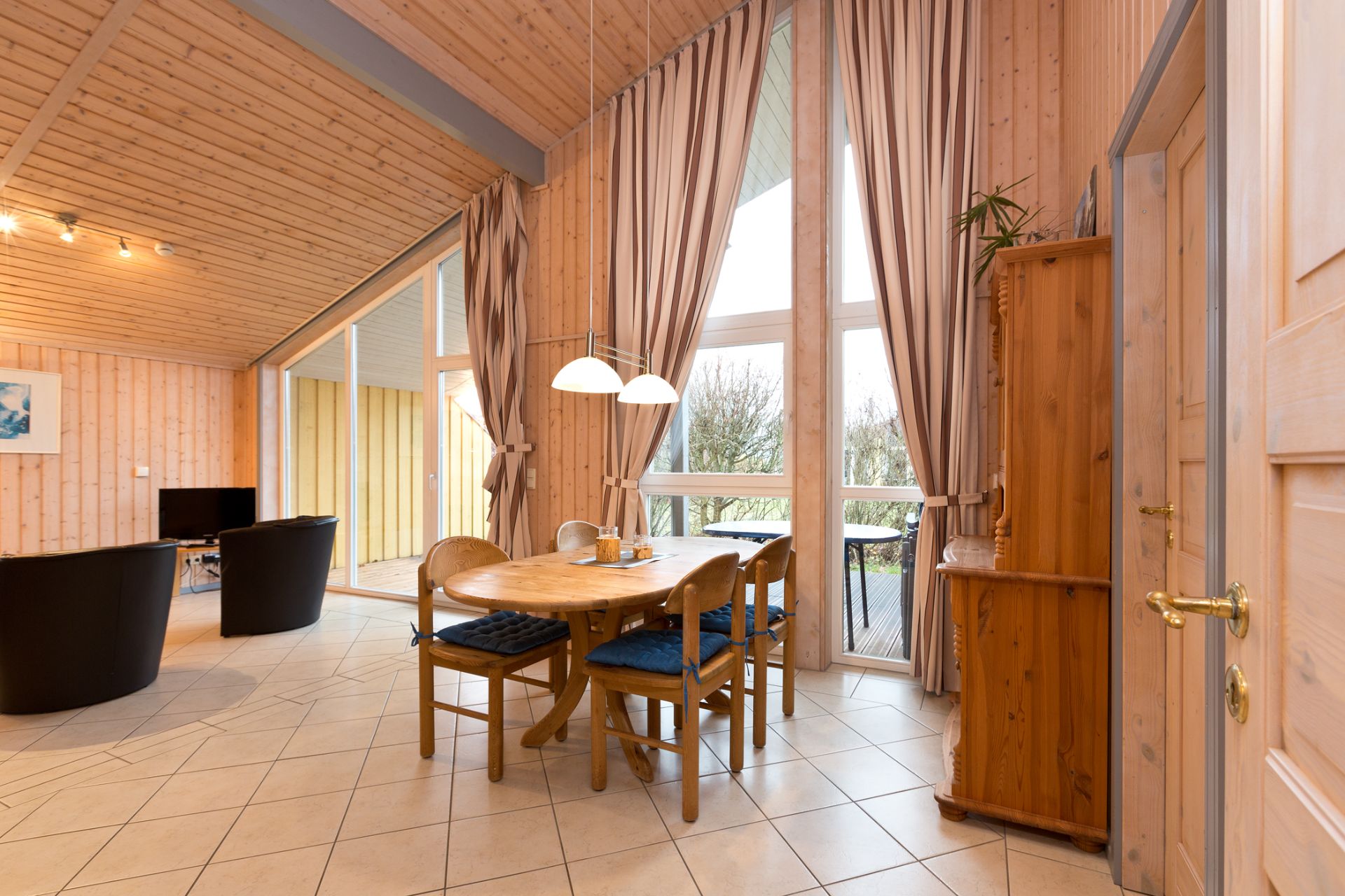 Essbereich mit Holztisch, vier Stühlen, großen Fenstern und Vorhängen in einem hellen Raum.
