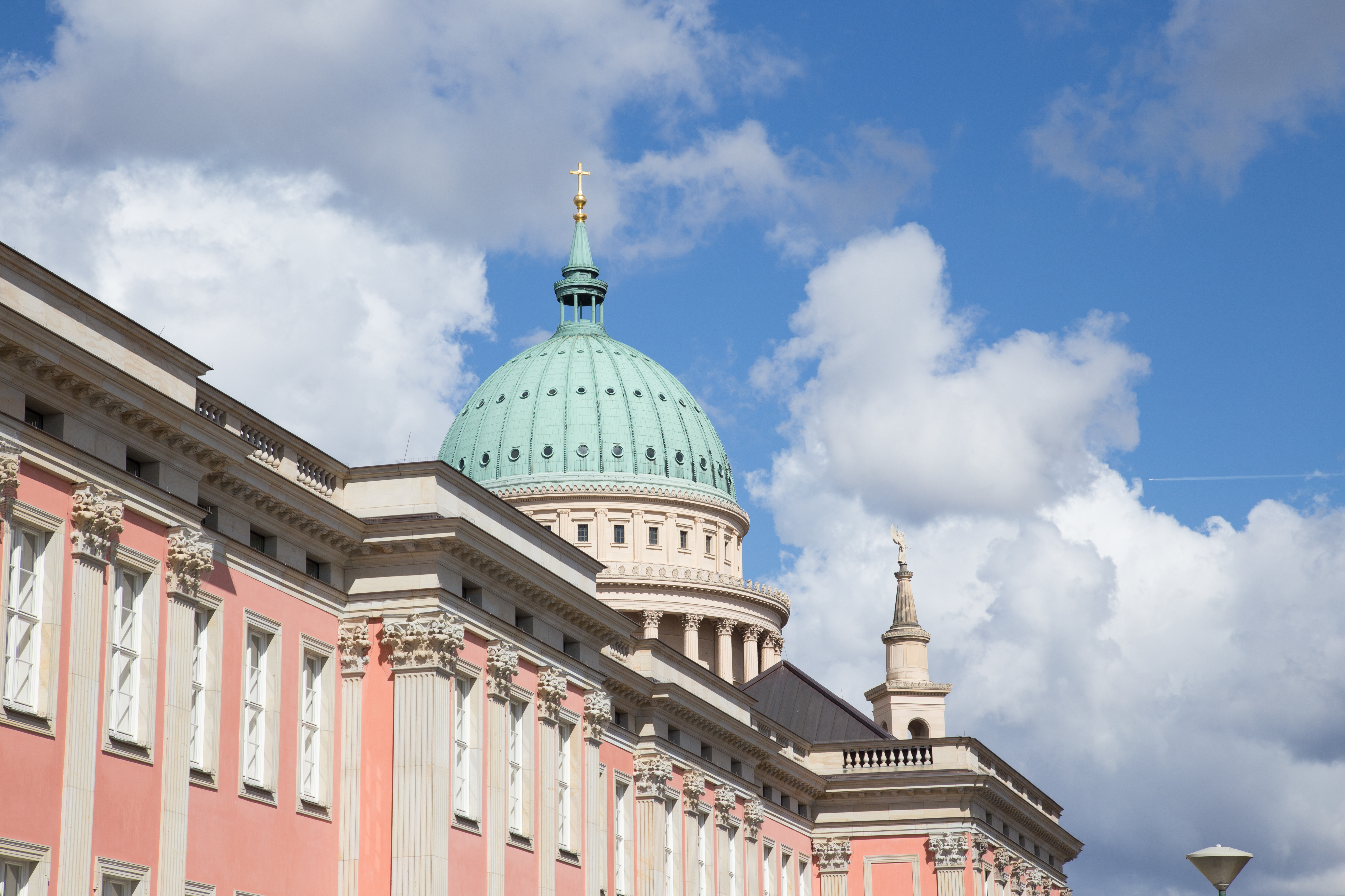 Großes Gebäude mit rosa Fassade und grüner Kuppel vor blauem Himmel.